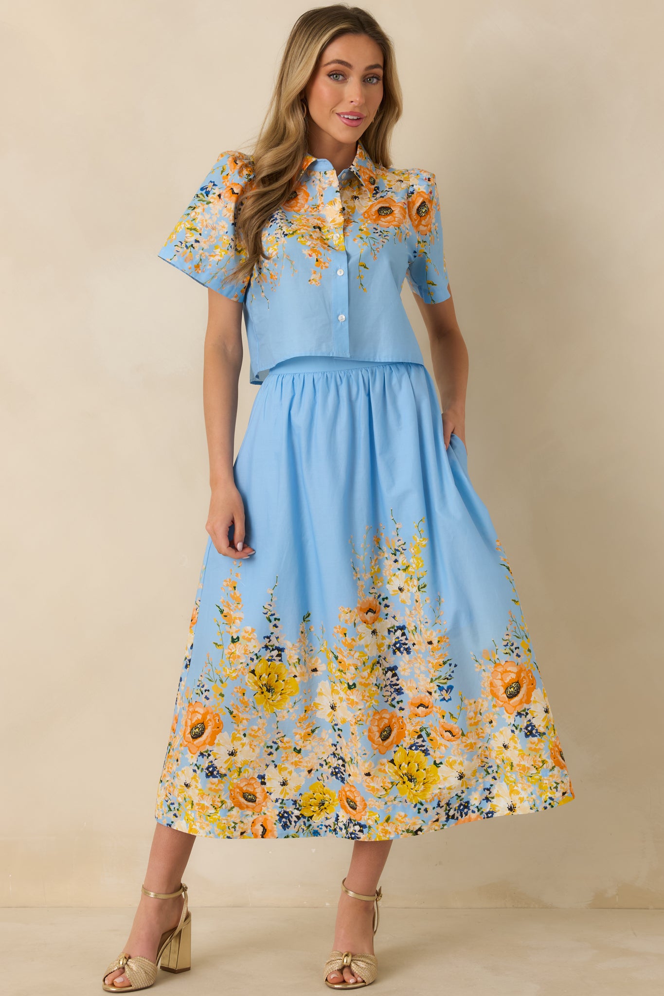 Blue cotton short sleeve top with a relaxed fit, collared neckline, button-down front, and multicolor floral print throughout.