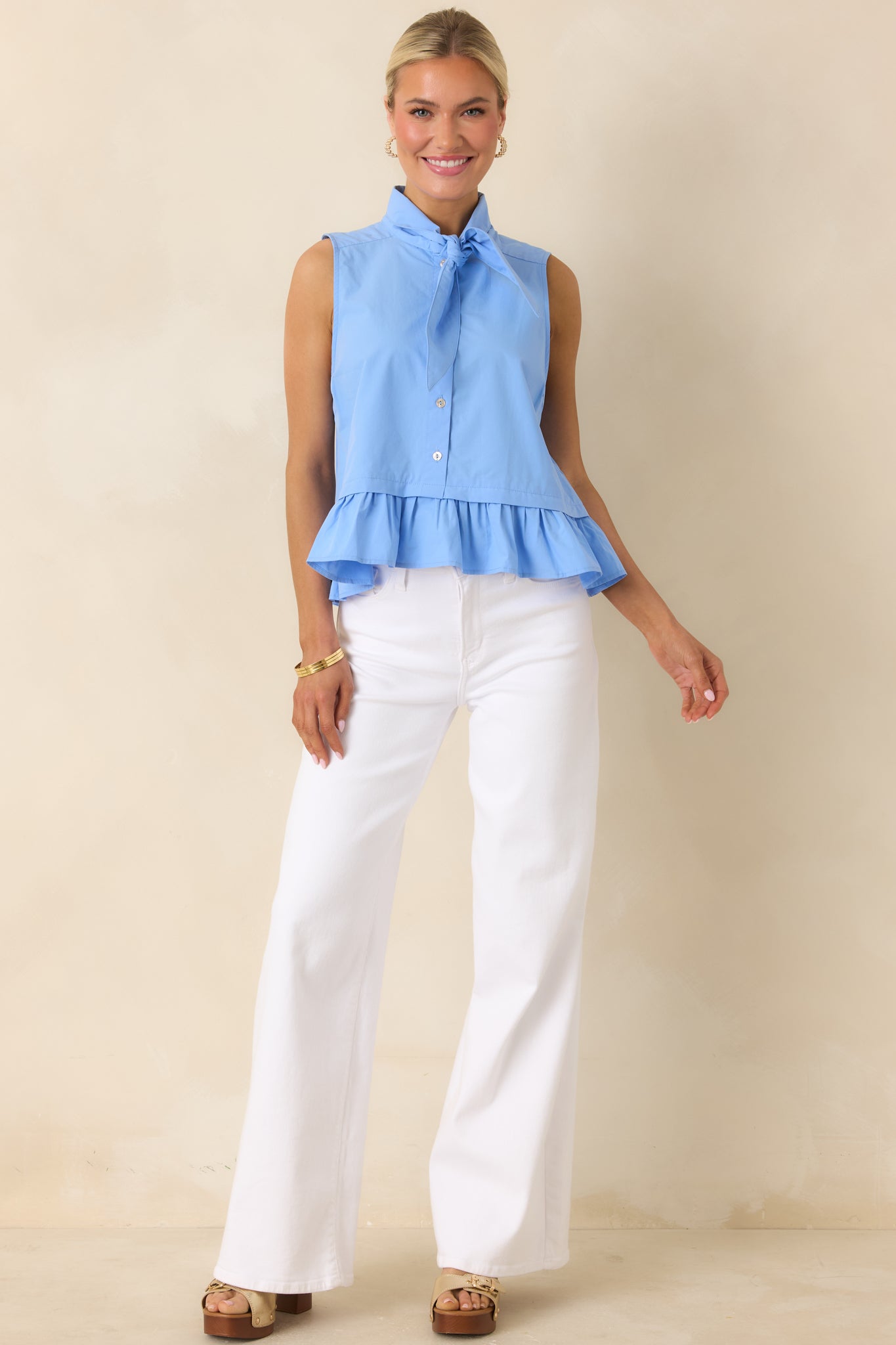 Blue cotton sleeveless top with tie neckline, button front, and softly gathered ruffle hem