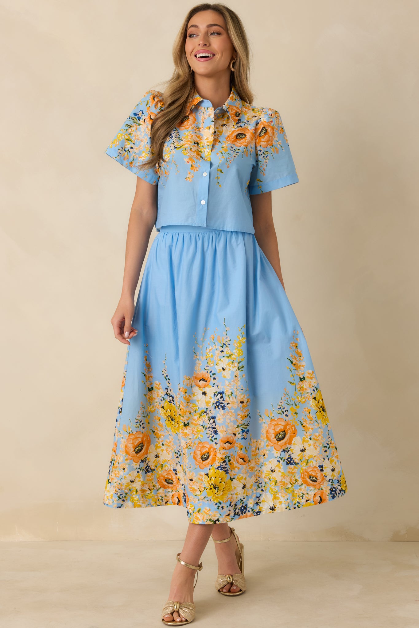 Blue cotton top designed with short sleeves, a polished collar, and an allover multicolor floral pattern.