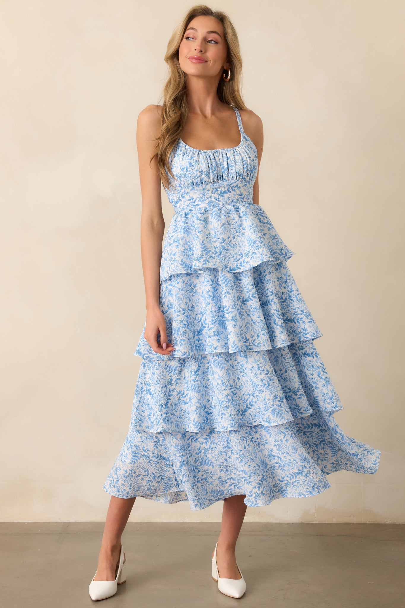 The blue floral maxi dress in a front-facing view, emphasizing the elastic scoop neckline, adjustable straps, and tiered skirt. The textured fabric adds dimension and flow.