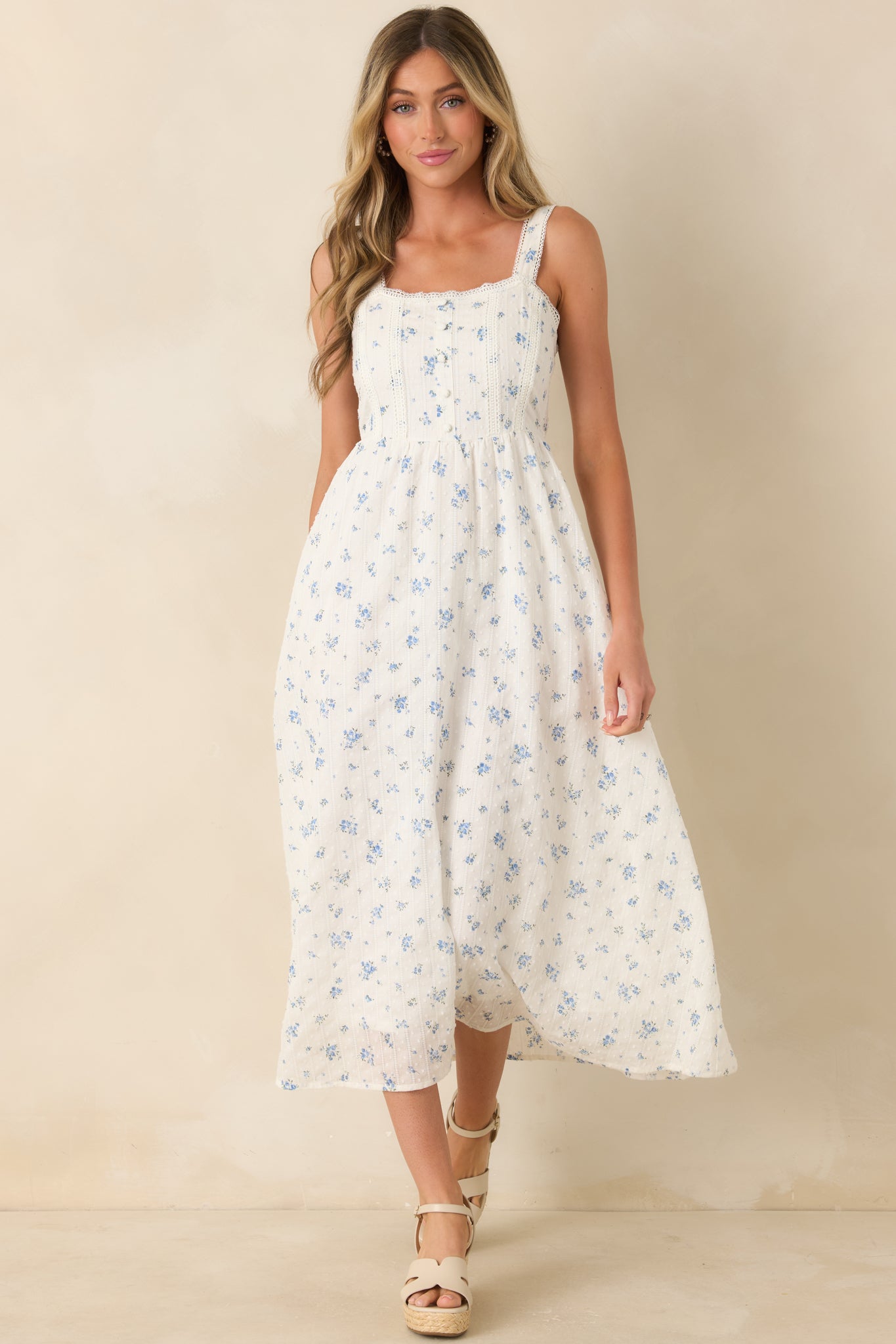 Blue floral midi dress featuring a covered button front, intricate lace insets, and a feminine flowing skirt design.