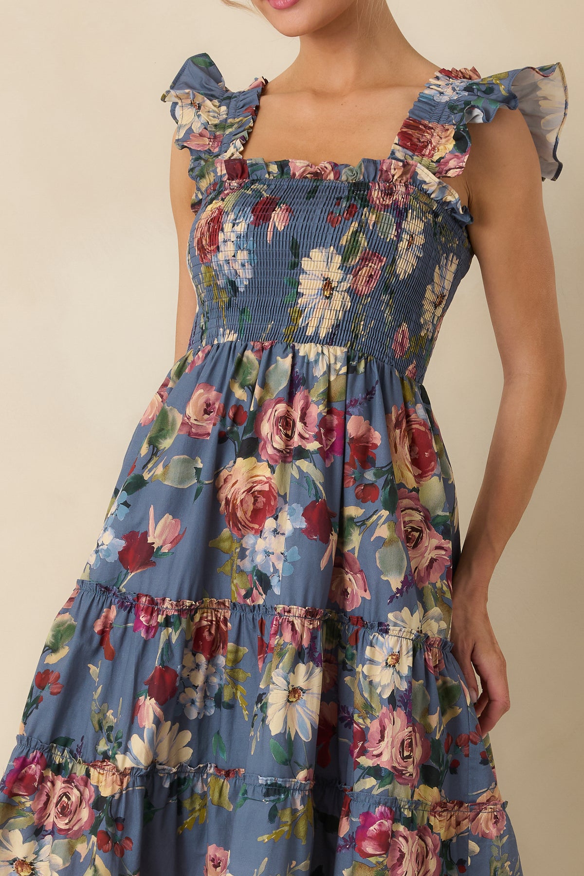 Close-up of a blue floral dress with a fully smocked bodice, square neckline, gathered trim, and ruffled shoulder straps.