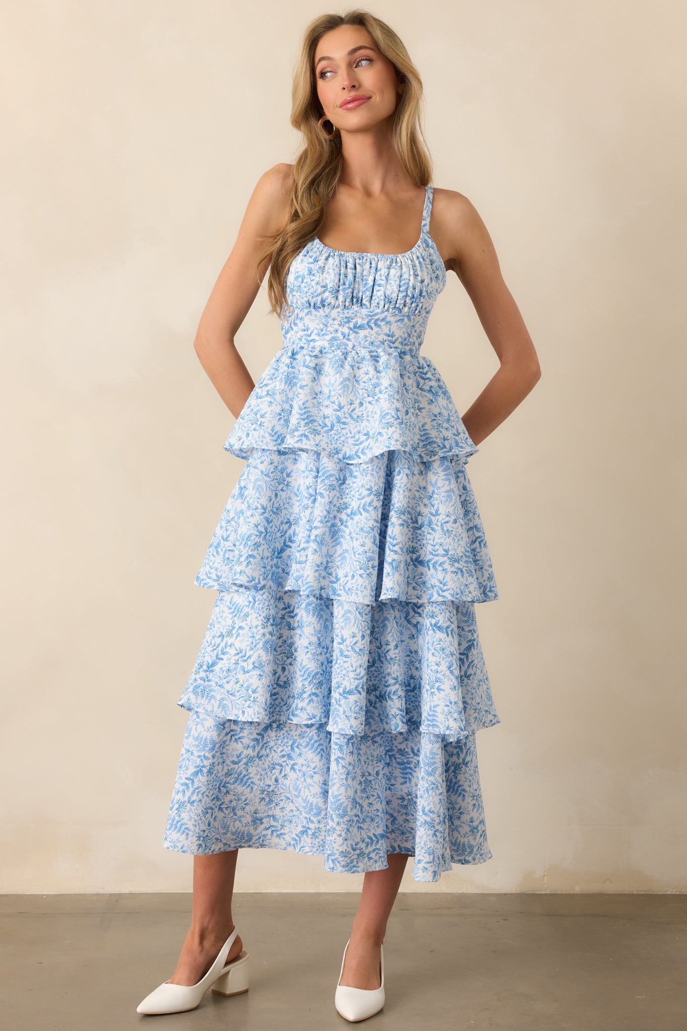 A full-body front view of a blue floral maxi dress featuring an elastic scoop neckline, adjustable straps, and a tiered skirt. The textured fabric creates a soft, flowing look.