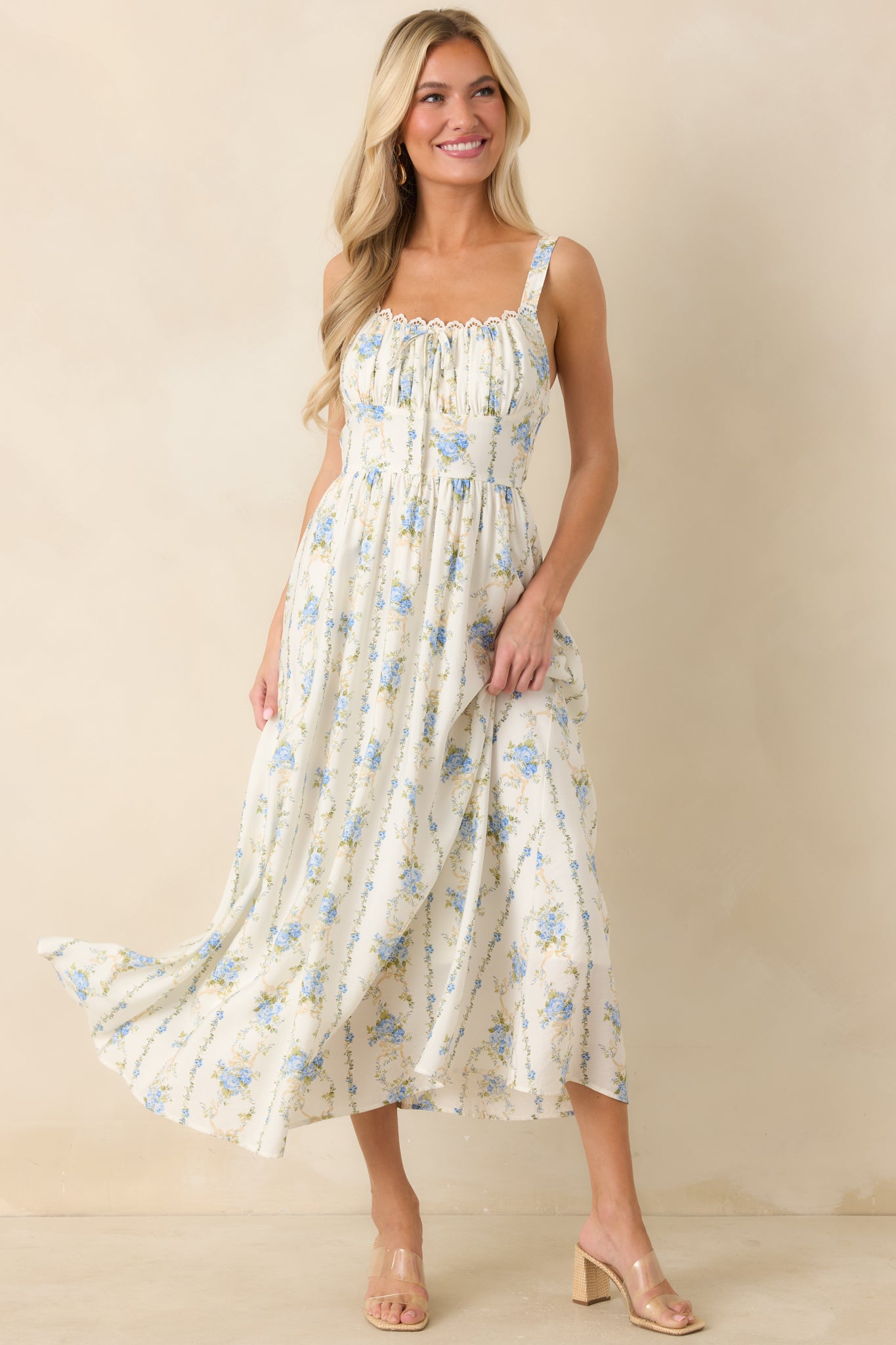 Blue floral midi dress with ruched neckline, lace trim detail, and a fixed bow accent centered along the bodice.