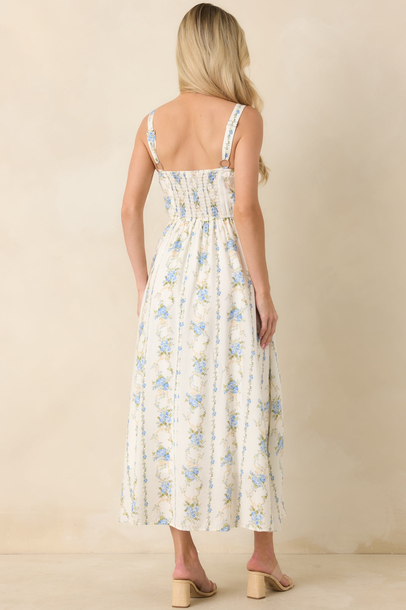 Rear view of blue floral midi dress highlighting smocked back panel, adjustable straps, and flowing skirt.

