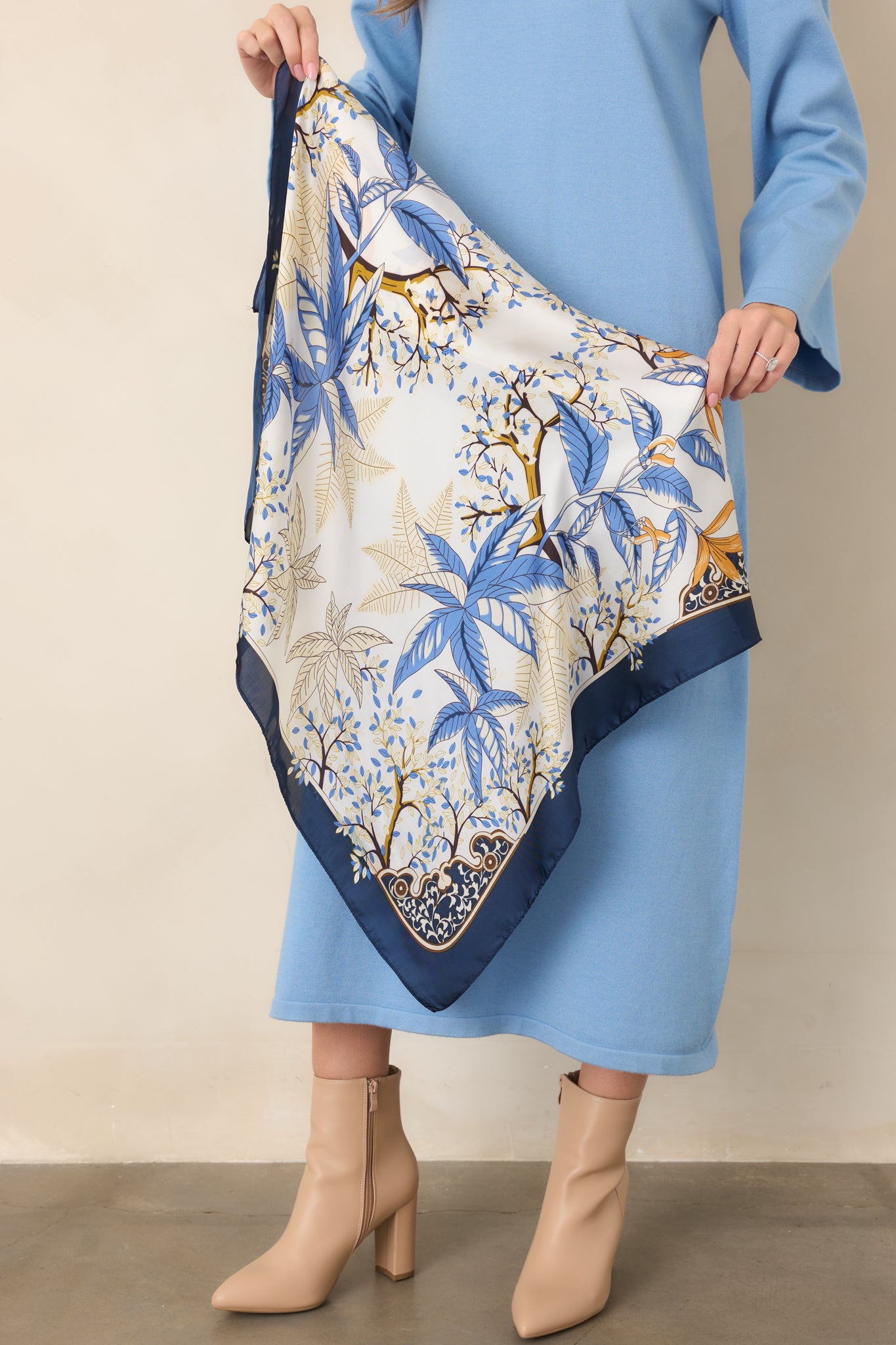 Scarf detail highlighting layered blue leaves, slender branches, and warm golden floral motifs within the intricate botanical pattern.