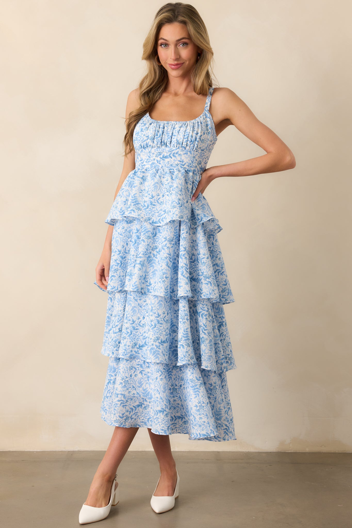 Front-facing view of the blue floral maxi dress, highlighting the elastic scoop neckline, adjustable straps, and the gentle layers of the tiered skirt. The textured fabric enhances the overall appearance.