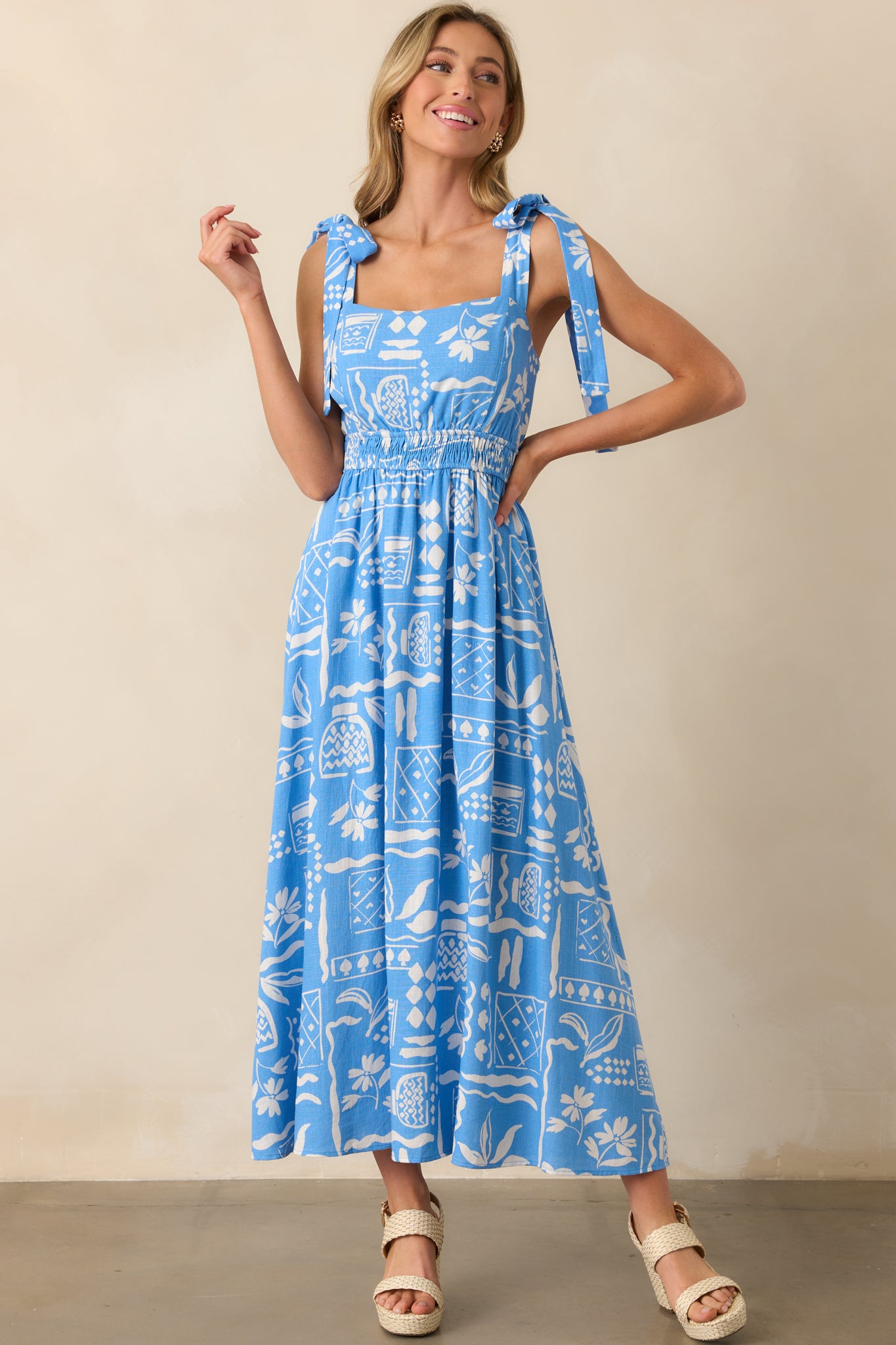Full body view of blue maxi dress with ivory tropical print, self-tie shoulder bows, and smocked waist.