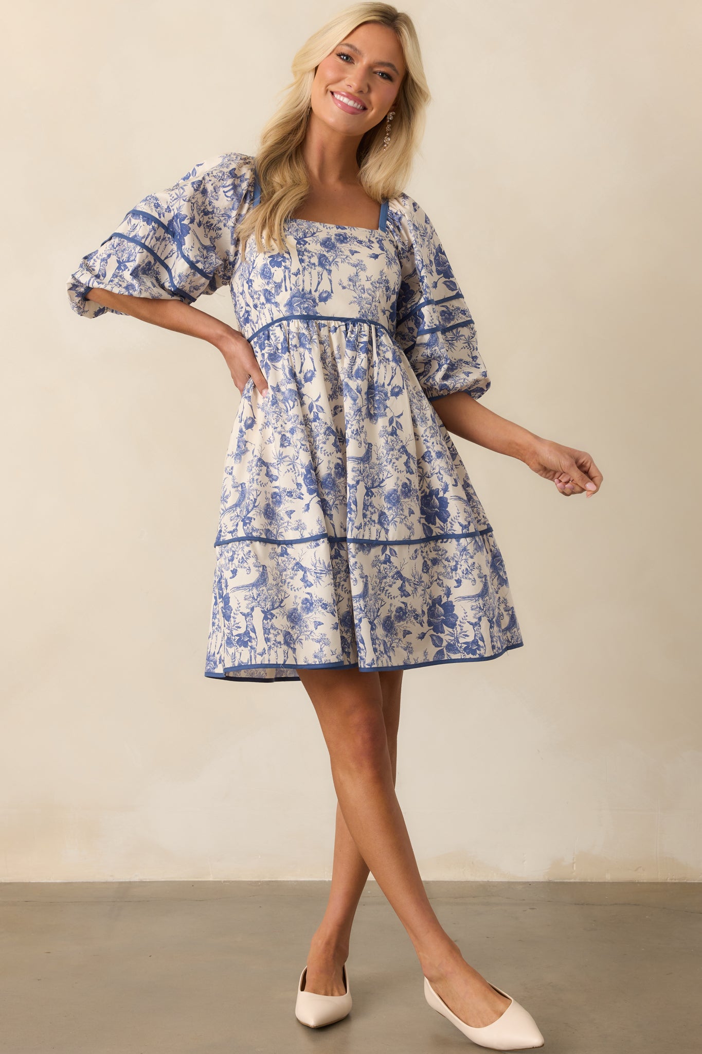 Full view of the blue mini dress showing its square neckline, puff sleeves, and softly flared tiered skirt with an allover toile floral print.