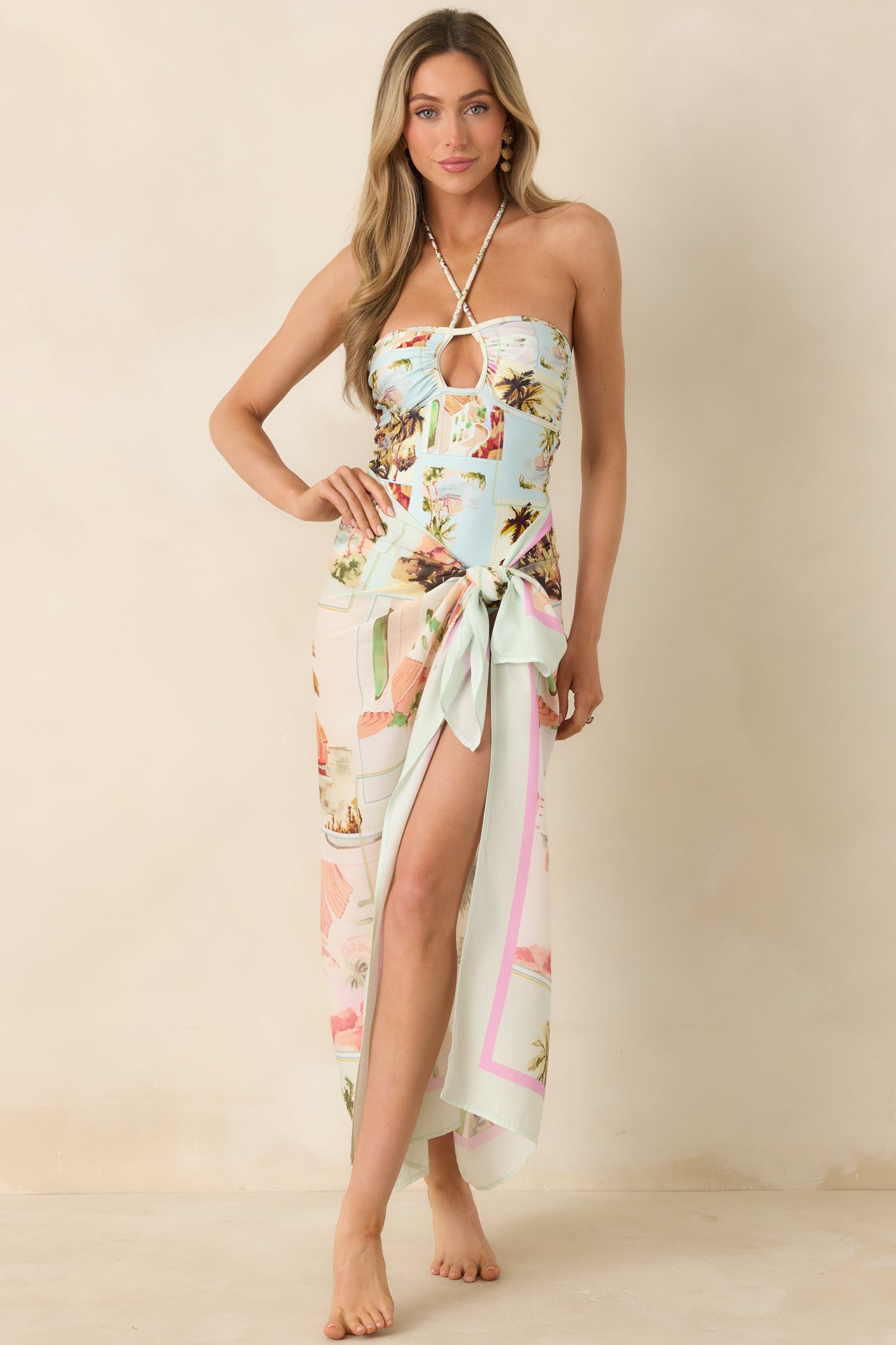 Blue one-piece swimsuit with multicolor scenic print and halter neckline.