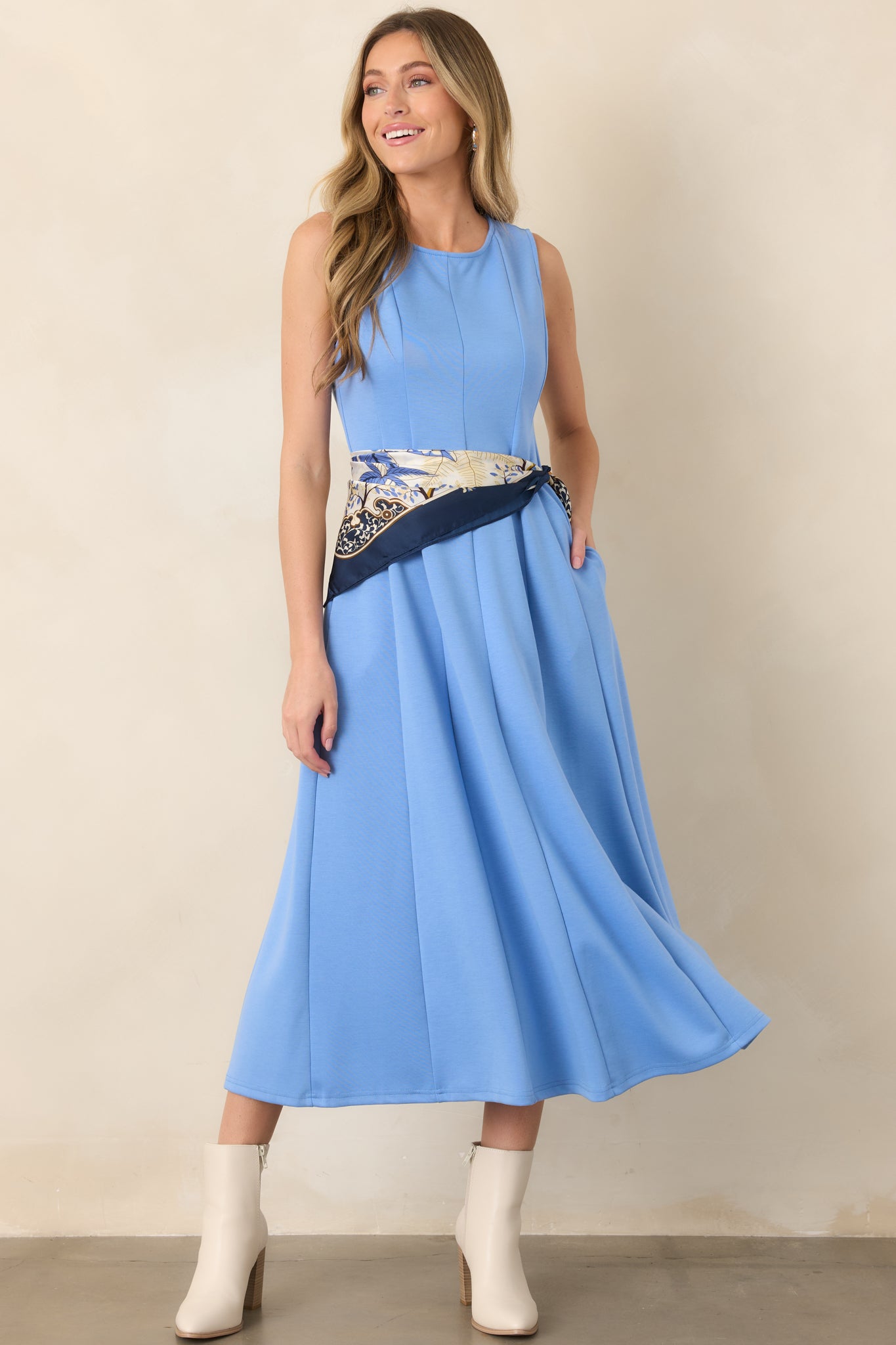 Blue midi dress showcasing a softly rounded neckline, sleeveless cut, smooth panel seams, and an easy silhouette with a gently flowing hem.