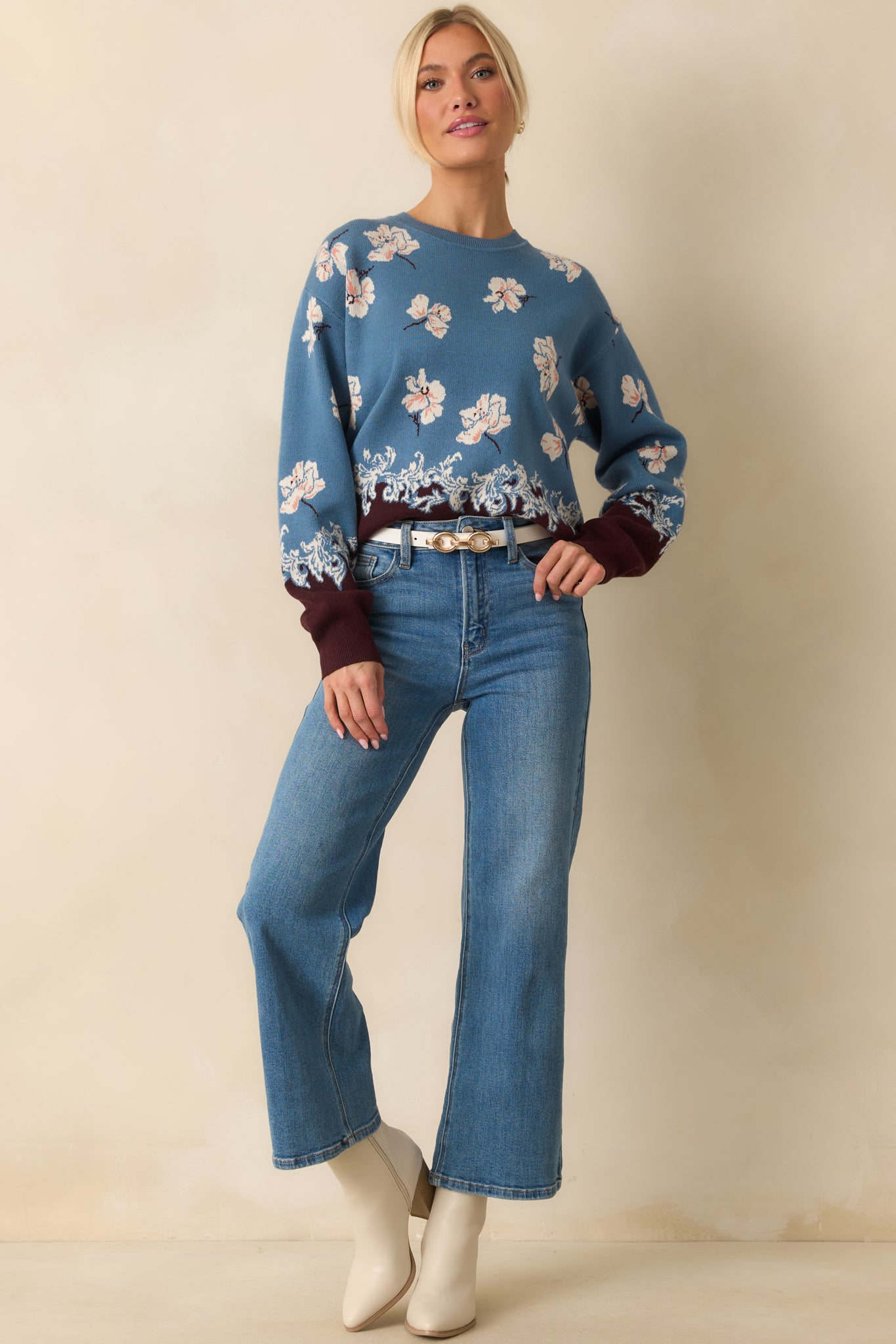 Blue sweater with ivory floral jacquard knit, crew neckline, and brown contrast hem featuring an ornate border pattern.