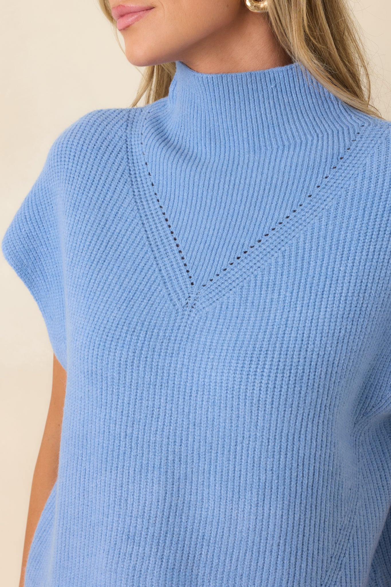 Detailed view of the blue sweater, emphasizing the ribbed knit texture, mock neckline, and intricate chest detailing.