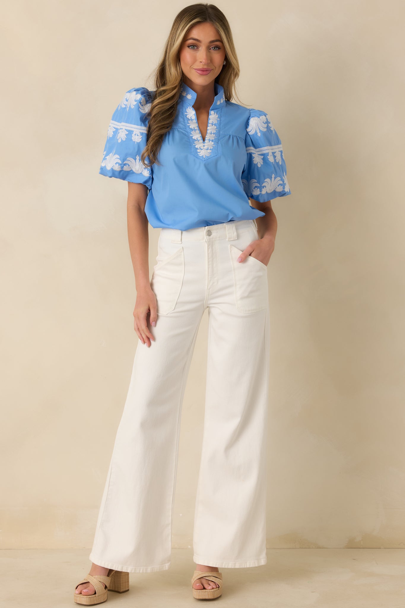 Front view of a blue top with a V-neckline, white embroidered accents, and short puff sleeves with gathered volume.