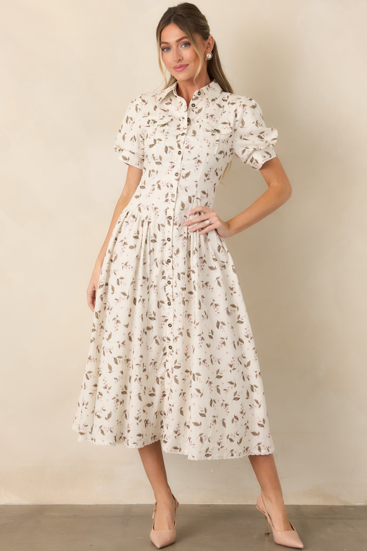 Blush flowers and muted leaves complement the pointed collar, puff sleeves, and polished button-front design of the ivory dress.