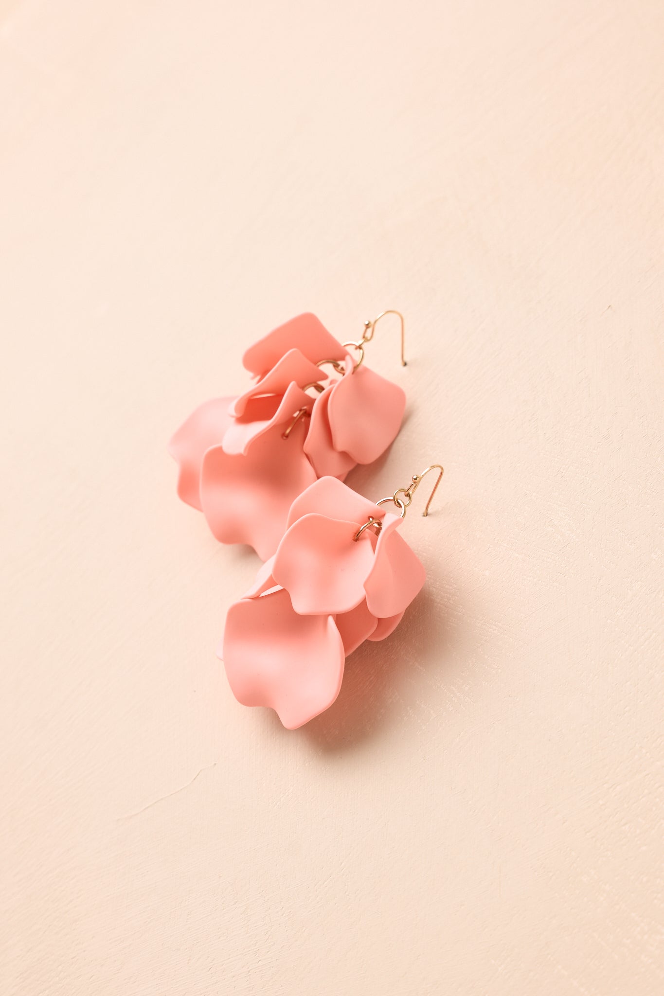 Angled view of blush pink earrings on beige backdrop highlighting matte finish and gold-tone accents.