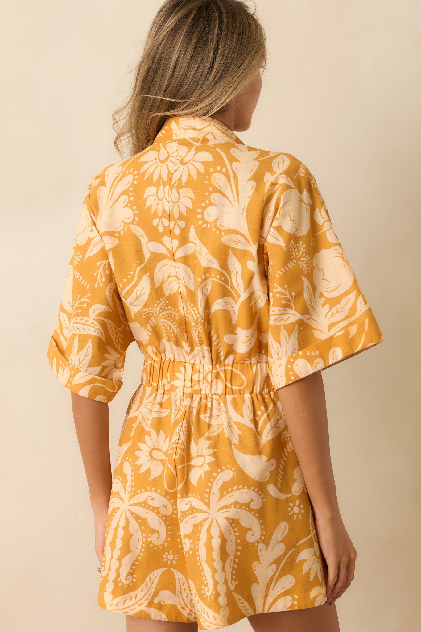Botanical damask romper highlighting the elasticized waist, relaxed short sleeves, and streamlined silhouette from behind.