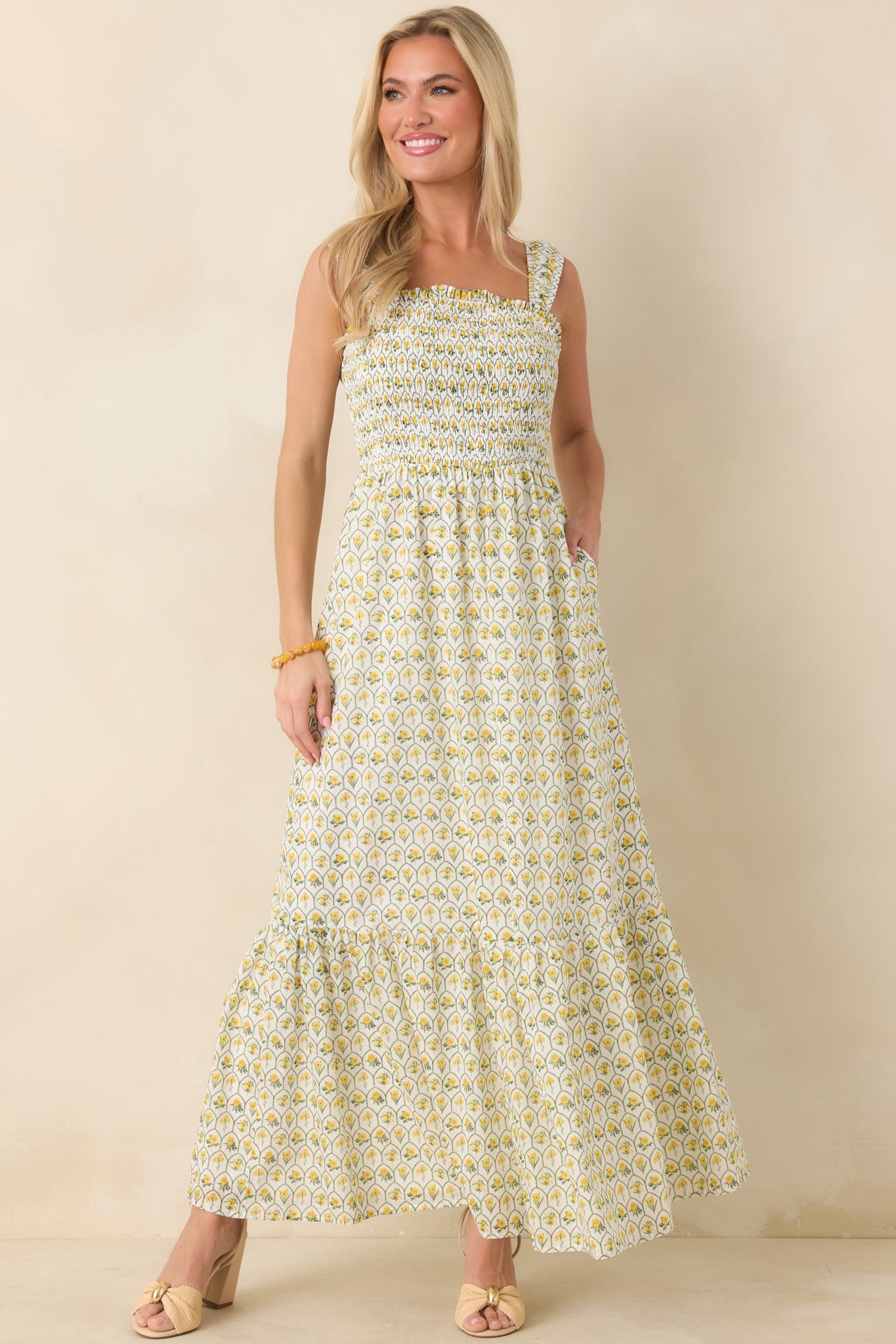 Bright floral maxi dress with square neckline, elastic smocked bodice, and flowing tiered skirt designed with hidden side pockets.