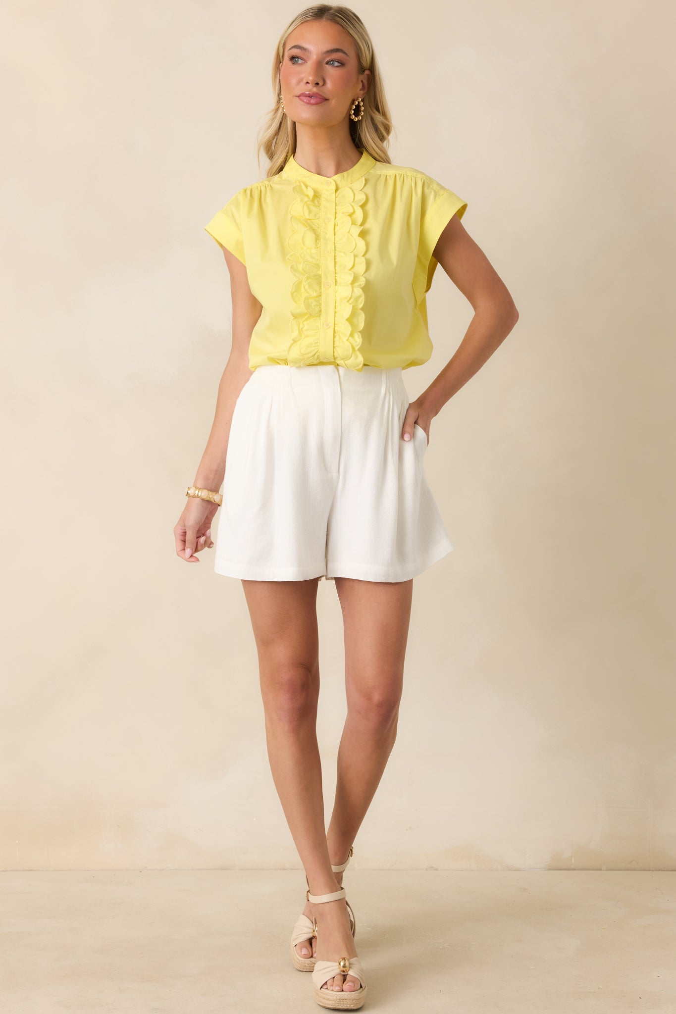 Bright yellow top with a structured band collar and decorative scalloped ruffle trim running down the front, finished with cuffed cap sleeves.