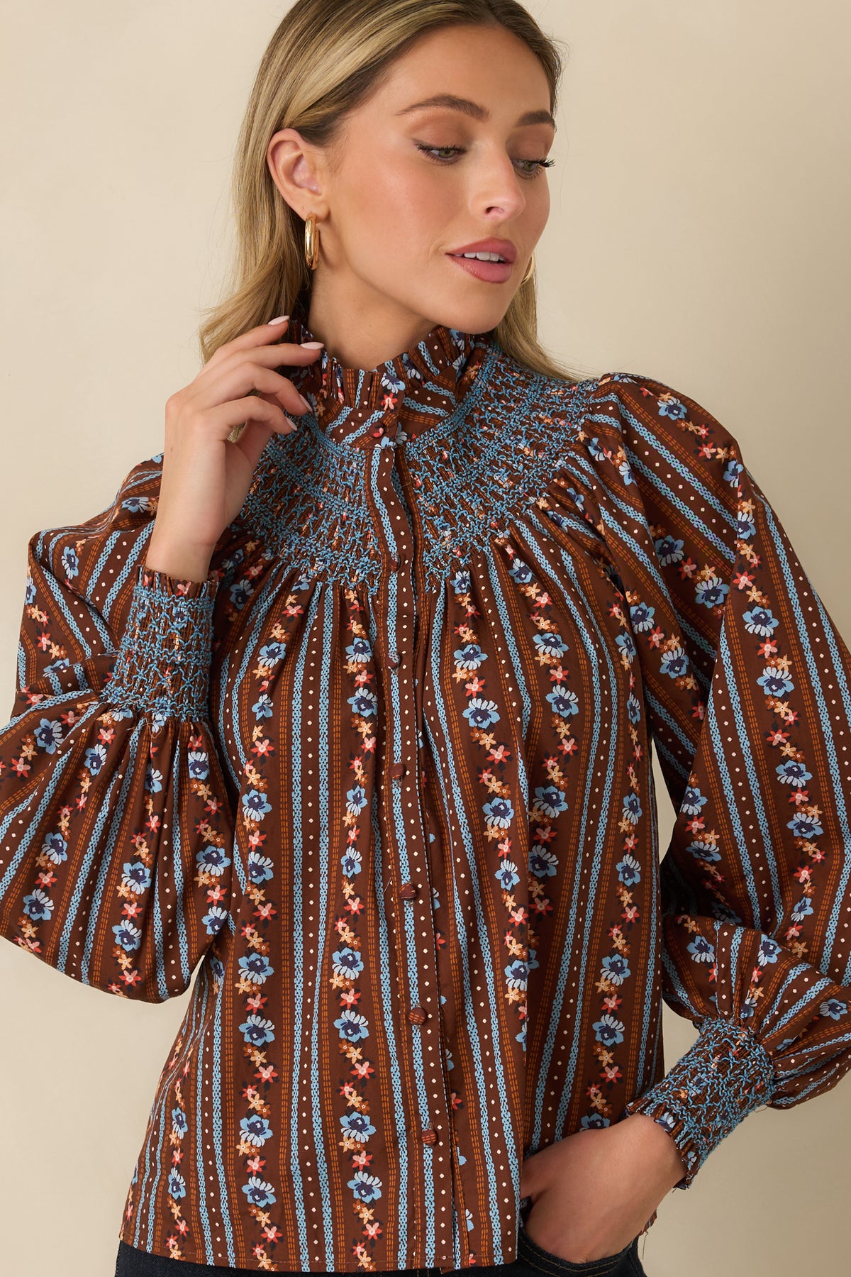 Petite blue and orange florals decorate this brown blouse, complemented by contrasting blue smocking and gentle gathers.