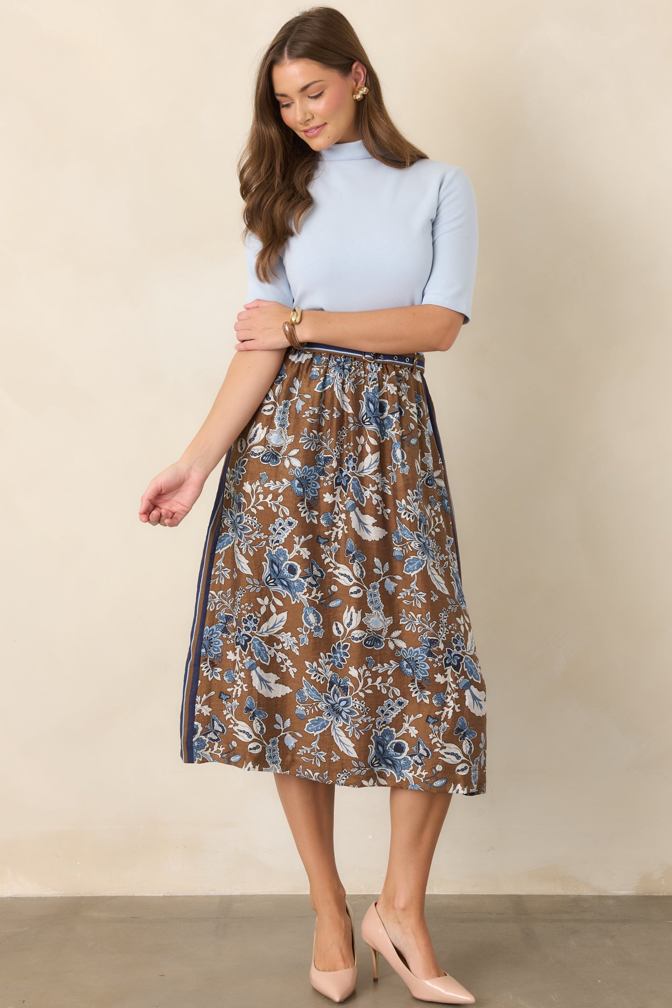 Rich brown floral midi skirt decorated with shades of blue, featuring a contrasting striped border, coordinating double-buckle belt, high-rise waist, and flowing A-line silhouette.