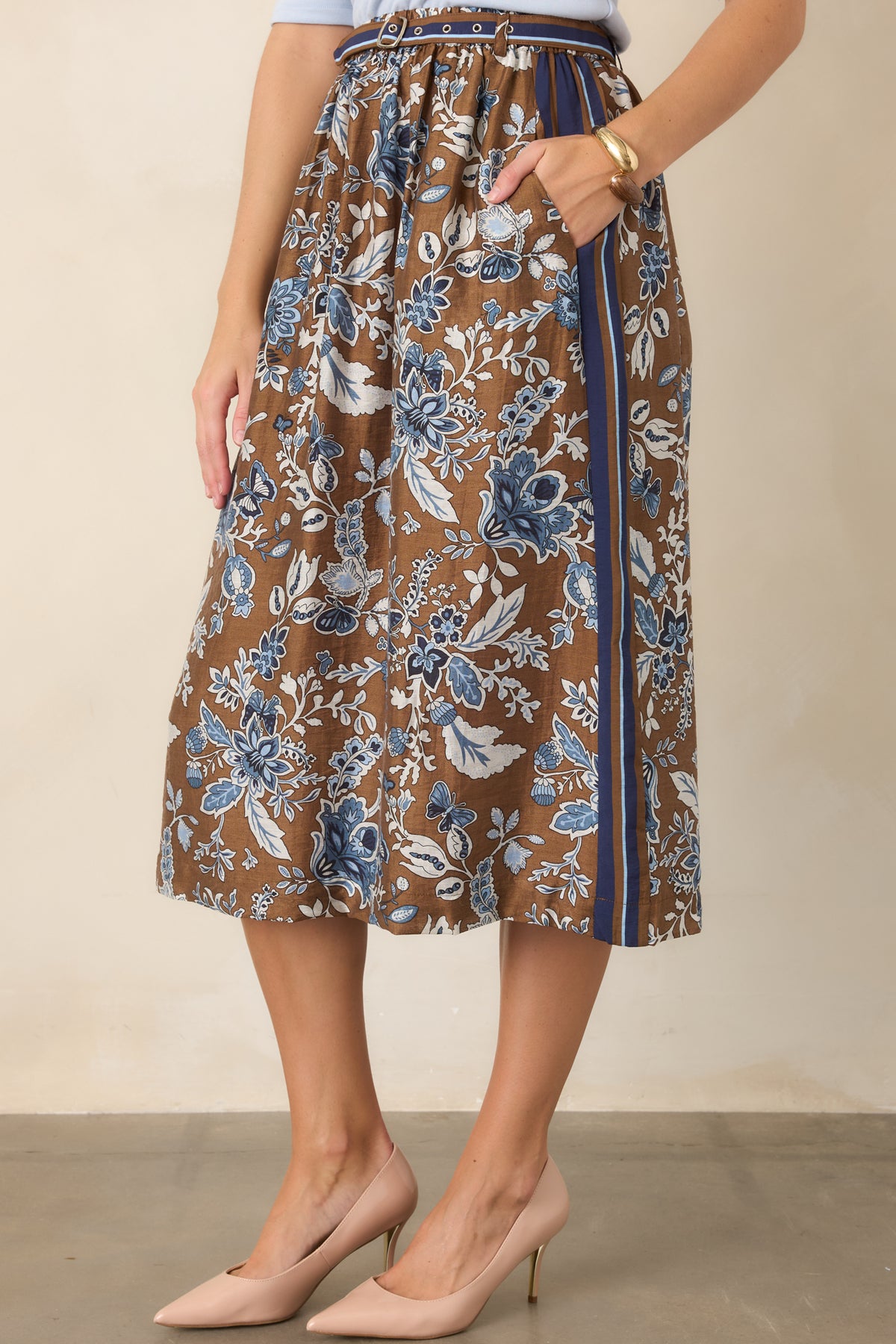 High-rise brown skirt showcasing blue floral detailing, a striped waistband, and coordinating double-buckle belt at the waist.