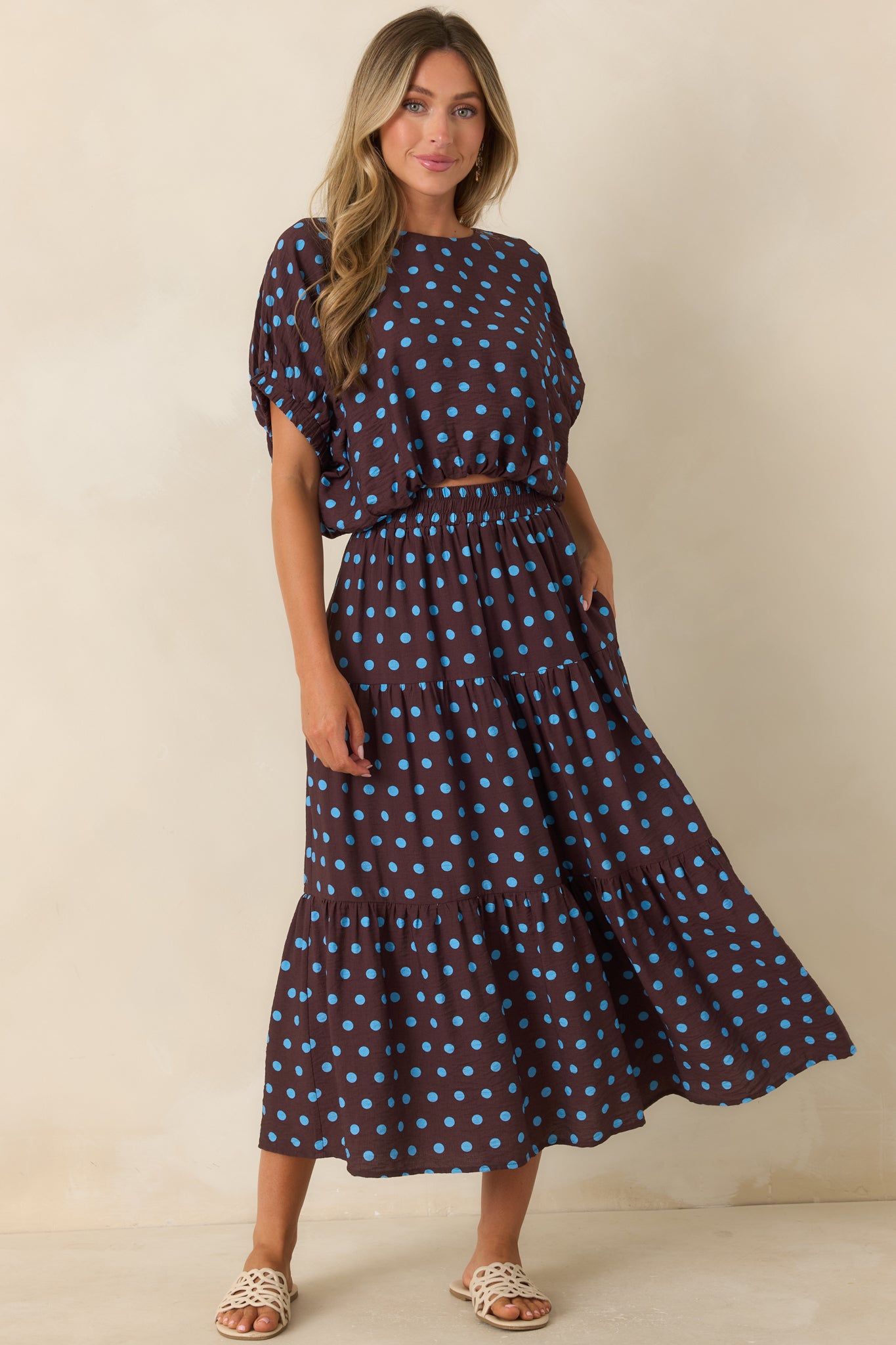 Brown flowy skirt featuring vibrant blue polka dots, a smocked elastic waistband, tiered panels, and functional side pockets.
