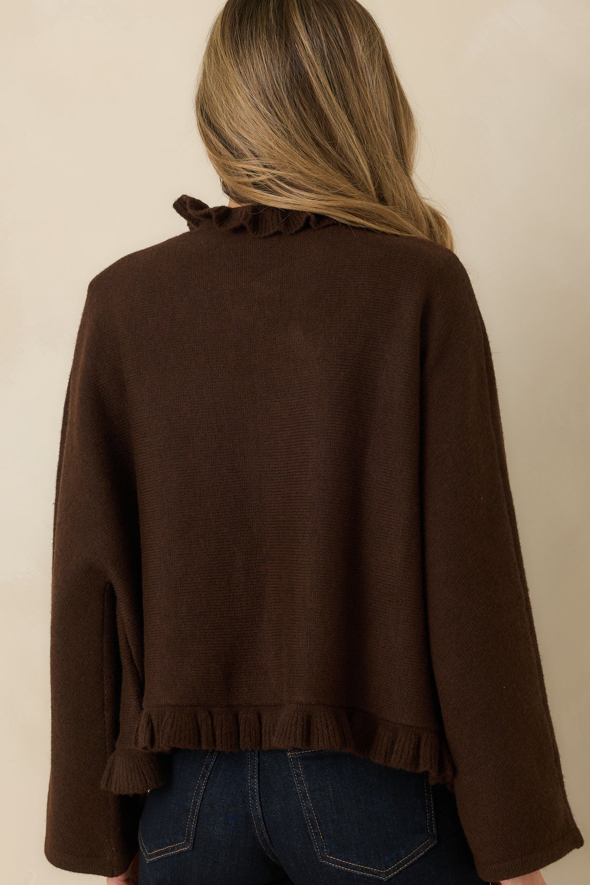 Back view of brown cape-inspired cardigan with a relaxed silhouette, wide sleeves, and ruffle-trimmed hem.
