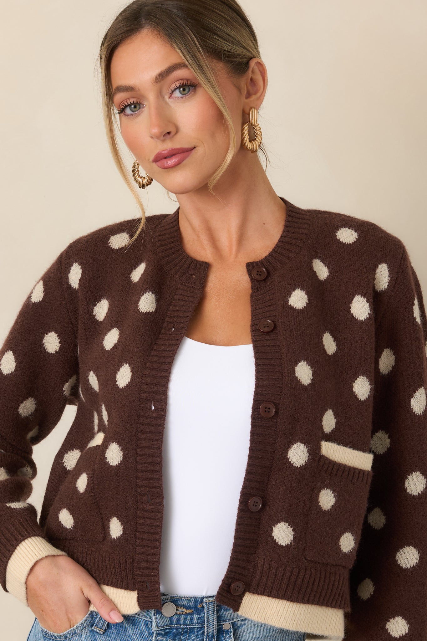 Brown knit cardigan showcasing the ivory polka dots, front patch pocket, ribbed edging, and layered ivory trim detail.
