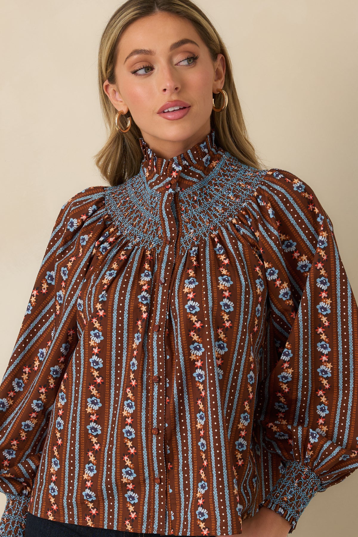 
Brown cotton blouse showcasing fabric-covered buttons extending down the front between delicate blue and orange floral stripes.