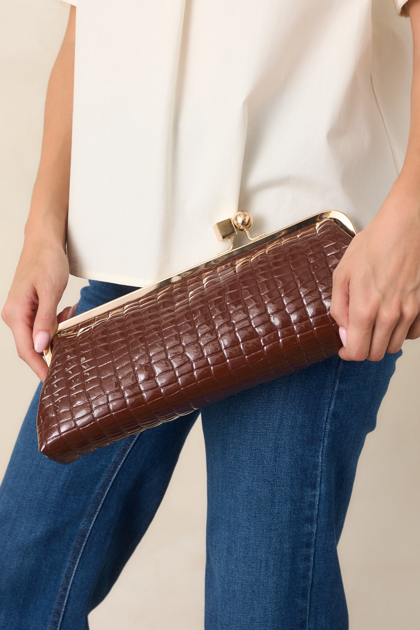 Brown rectangular clutch featuring croc-embossed faux leather, a gold-tone kiss-lock frame, and a structured silhouette with optional straps.