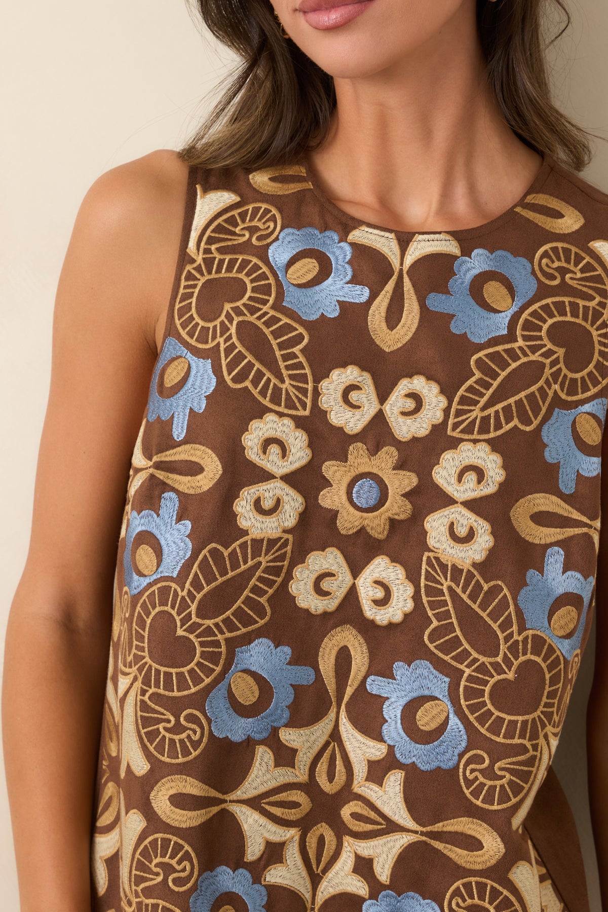 Close-up of the brown dress fabric featuring raised blue, ivory, and golden tan floral embroidery with curling stems and leaves.