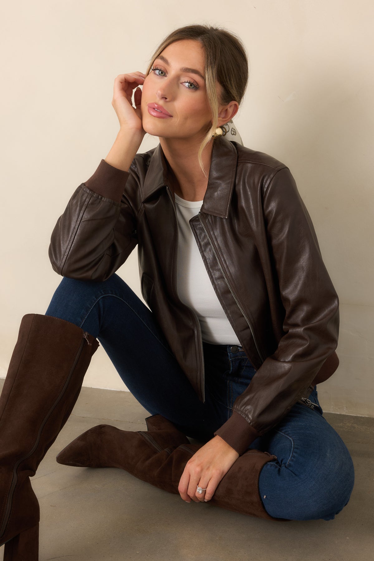 Smooth brown faux leather bomber jacket with a collared neckline, front zipper closure, welt pockets, ribbed cuffs, and matching hem.