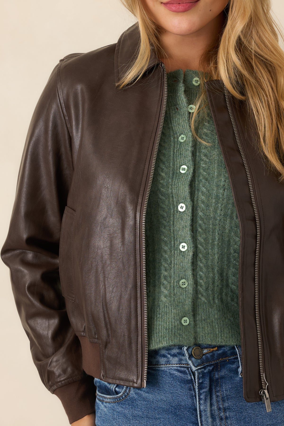 Brown faux leather jacket detail highlighting the smooth finish, front zipper, and ribbed knit trim.