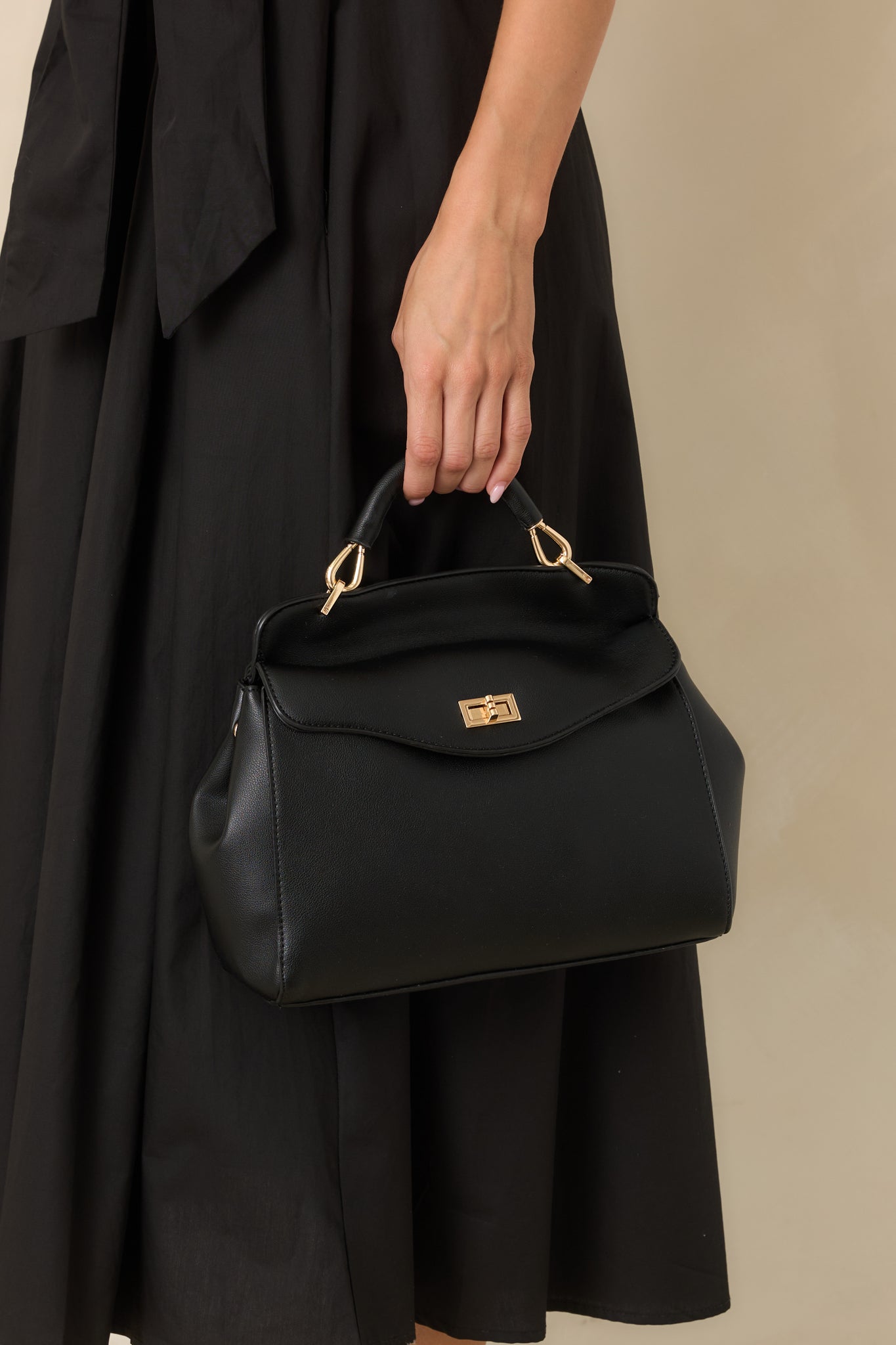 Brown faux leather handbag featuring a softly curved silhouette, gold-tone twist lock closure, top handle, and optional shoulder strap.