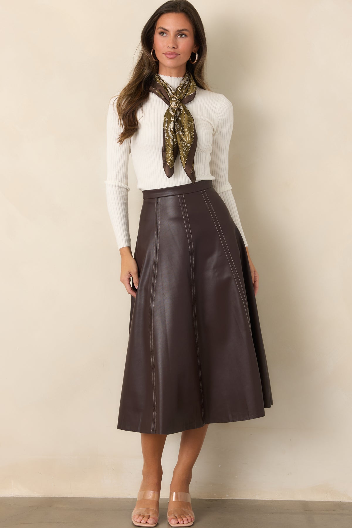 Rich brown faux leather skirt featuring a defined waistband, paneled construction, contrast stitching, and a flared A-line silhouette.