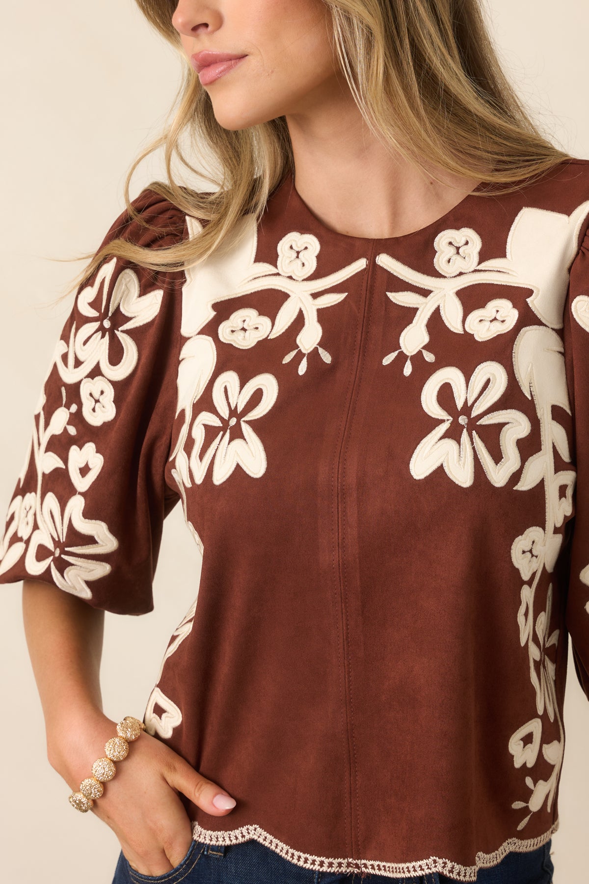 Close-up of ivory floral appliqués with embroidered detailing against the warm brown faux suede fabric.