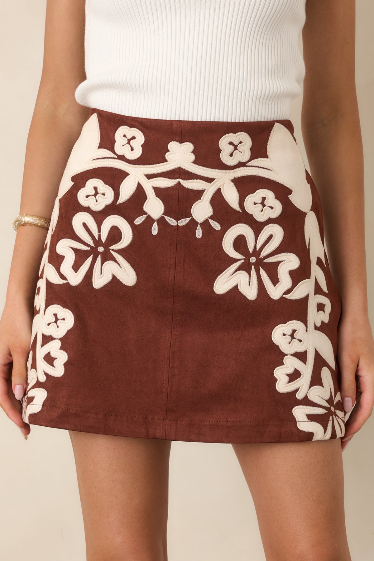 Close-up of the ivory floral appliqués winding across the textured brown faux suede front.