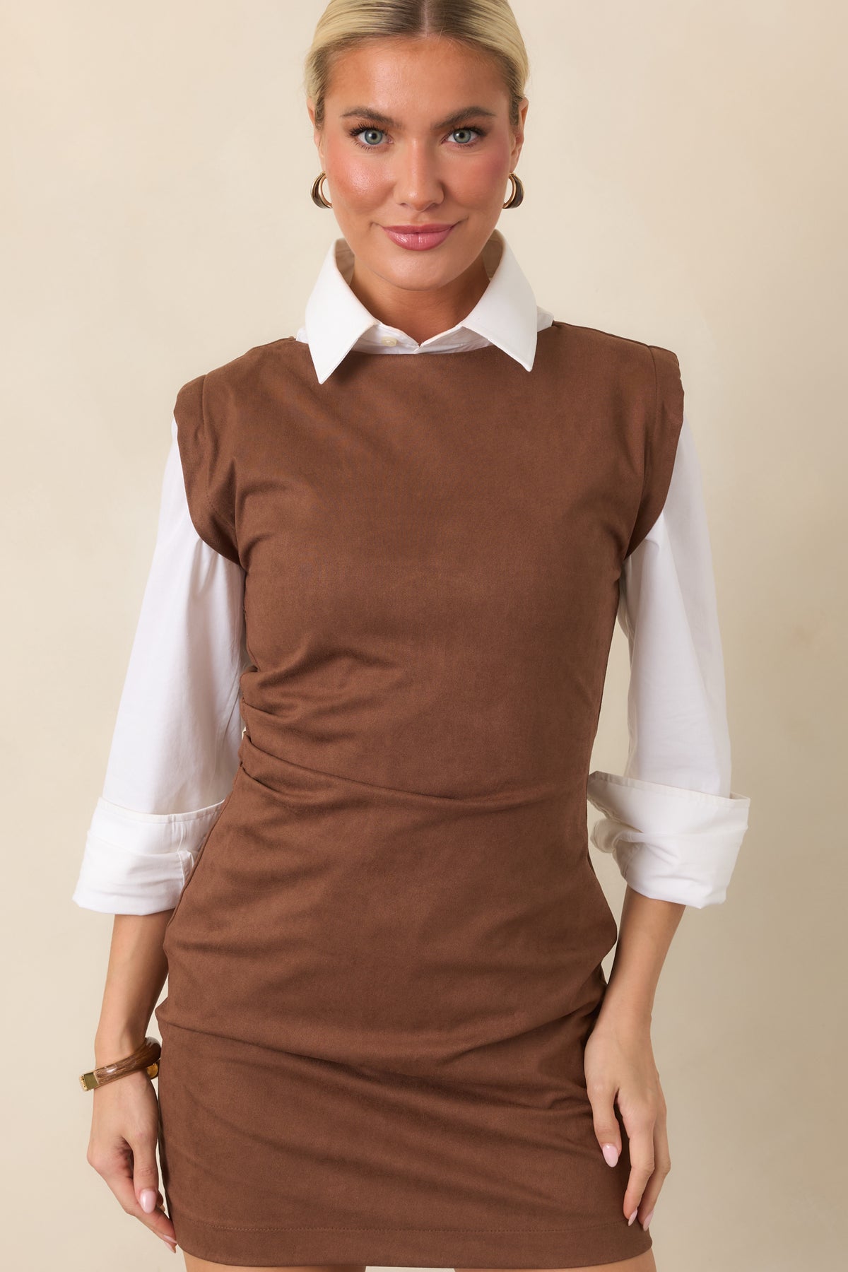 Round neckline and broad shoulders frame the fitted brown silhouette with softly gathered waist detailing.