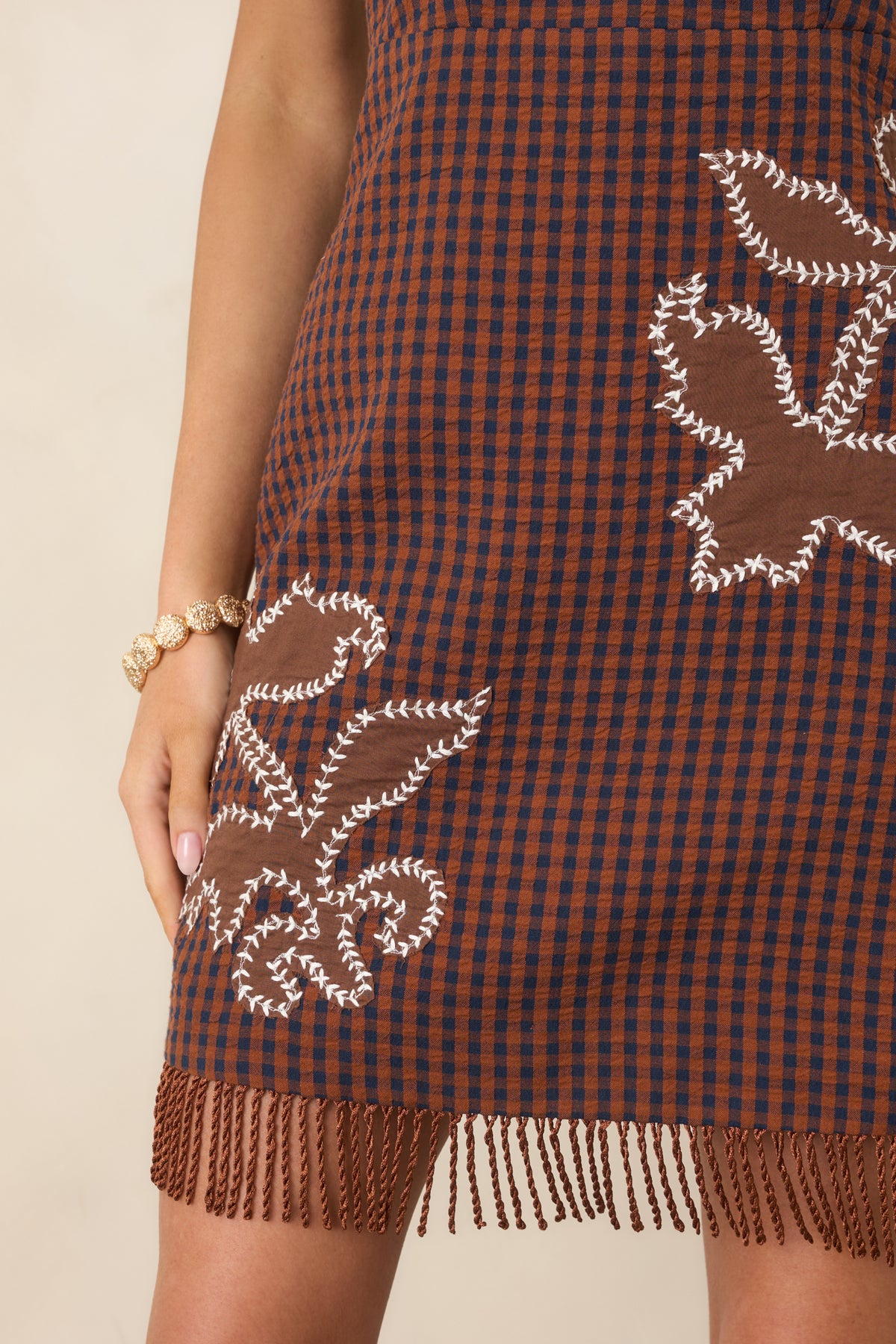 Close view of brown floral appliqués with ivory stitching against the rust and navy gingham fabric.