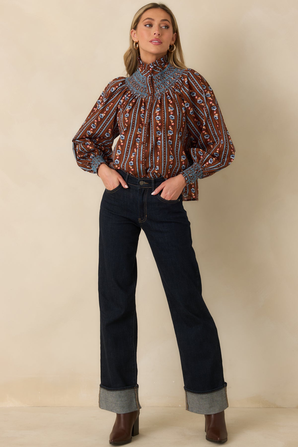 Brown floral blouse featuring a high ruffled neckline, blue smocked yoke, and gentle gathers beneath the neckline.