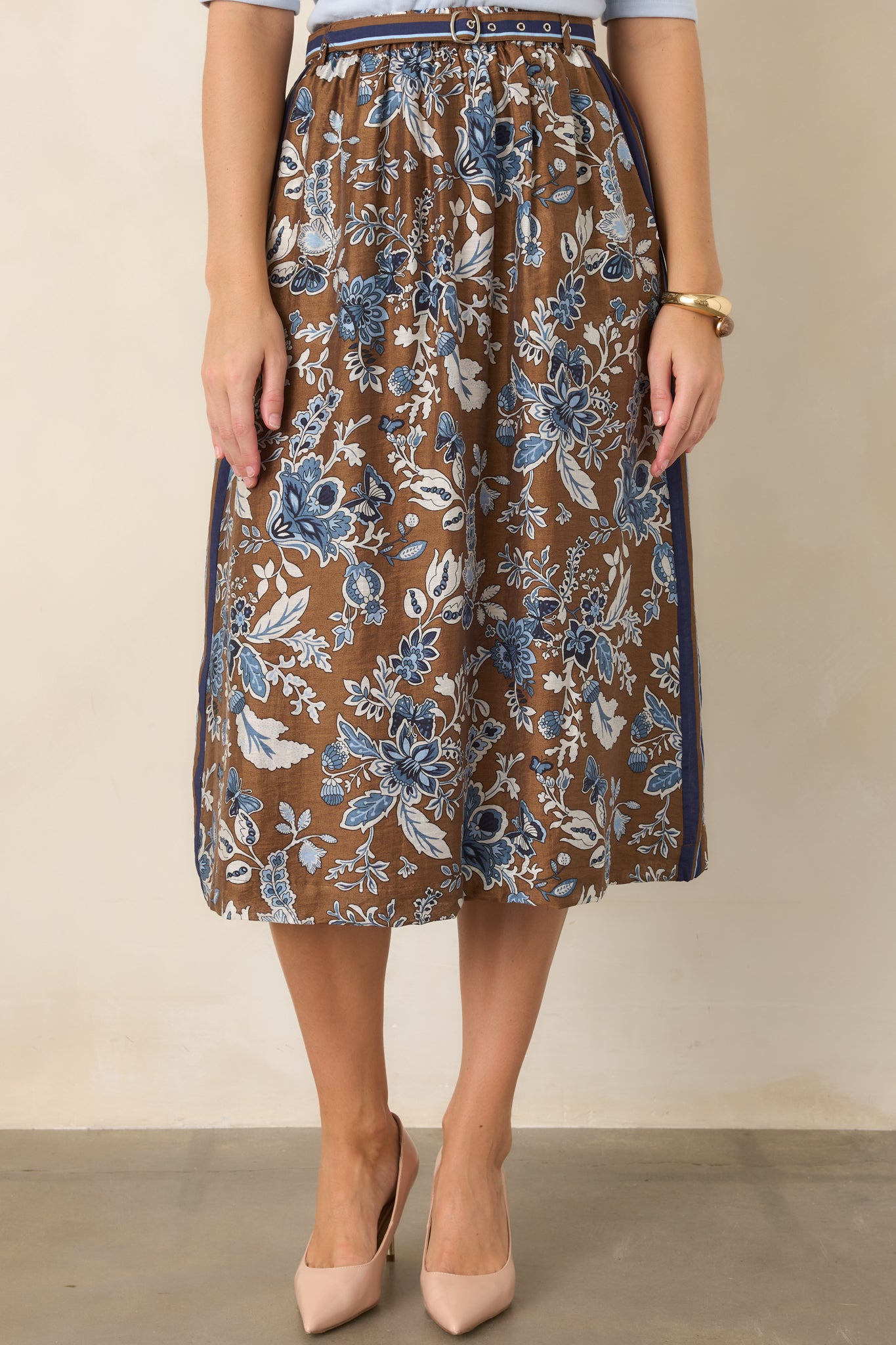 Brown floral skirt highlighting its contrasting striped border along the waistband and side, with blue botanical motifs throughout.