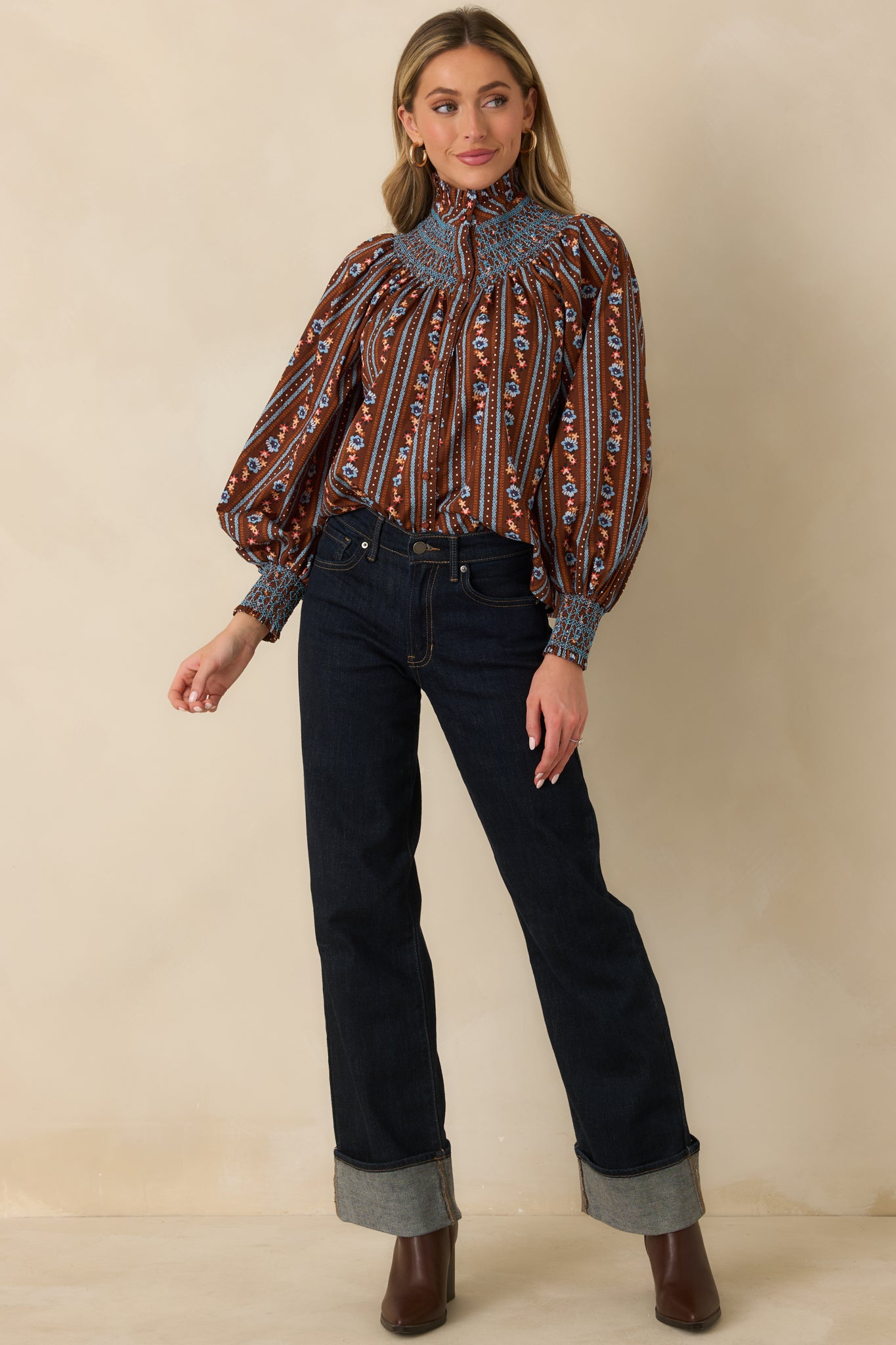 Brown cotton blouse featuring petite blue and orange florals arranged in vertical stripes, a high ruffled neckline, and long balloon sleeves.