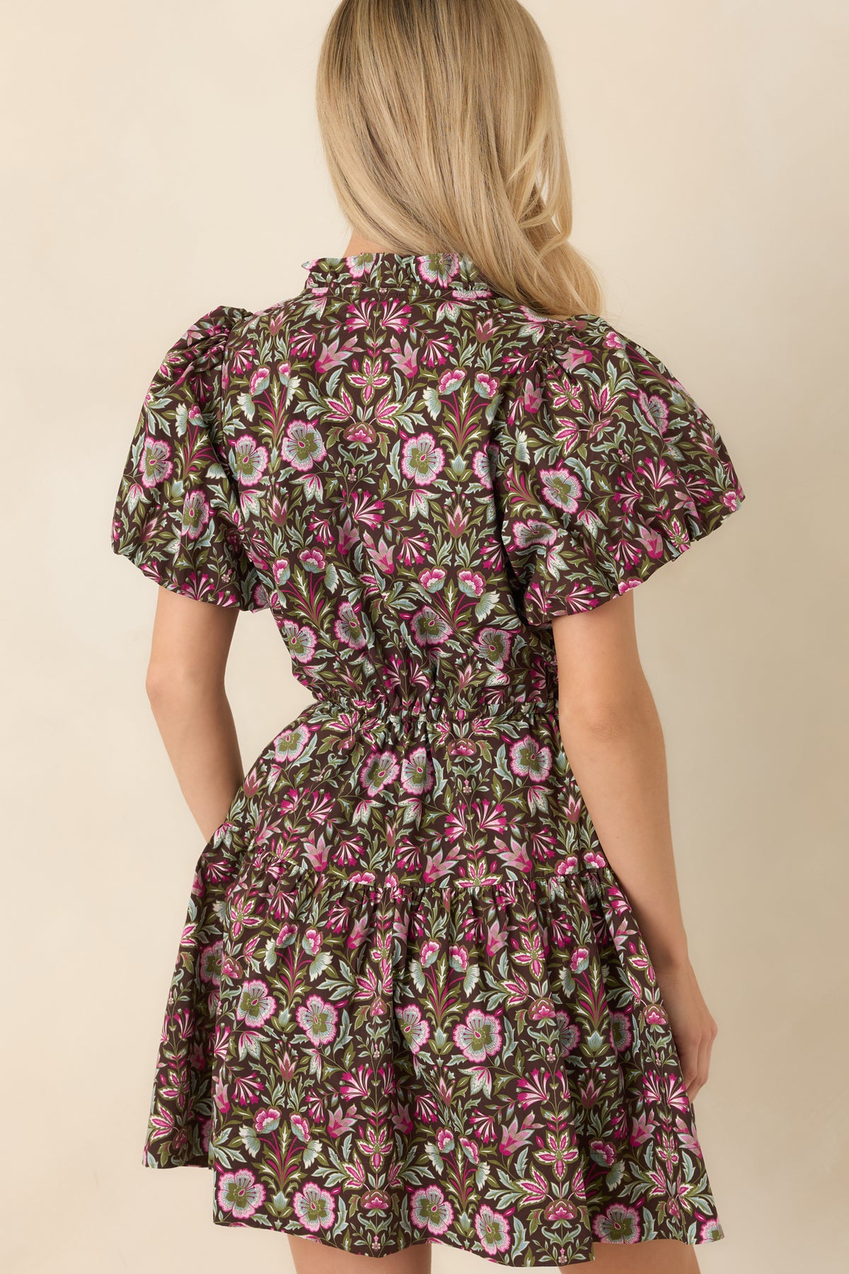 Rear view of the brown floral mini dress showcases its flutter sleeves, adjustable drawstring waist, and softly tiered skirt.