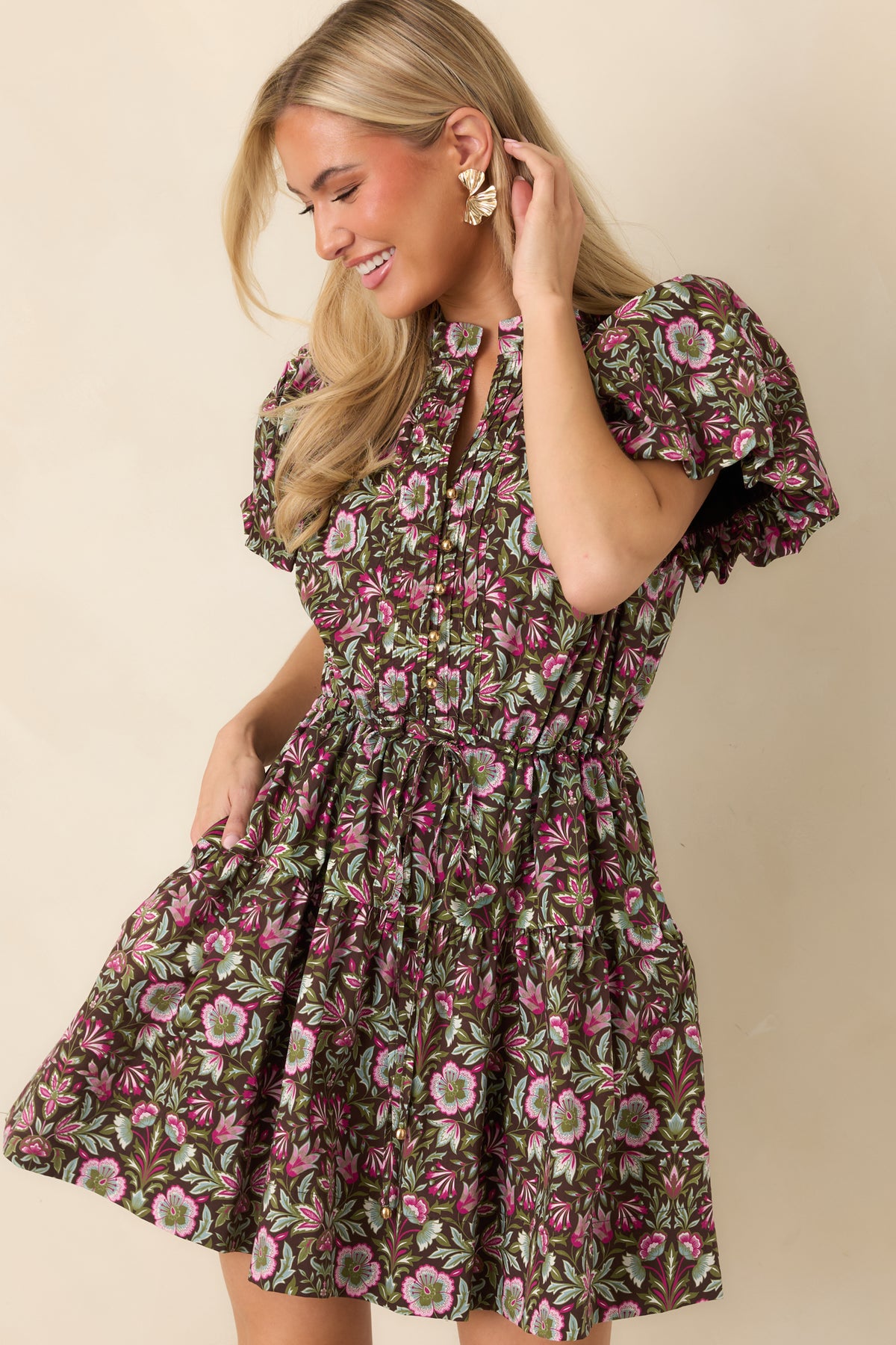 The brown floral mini dress features a softly tiered skirt with a flowing hem and functional side pockets.