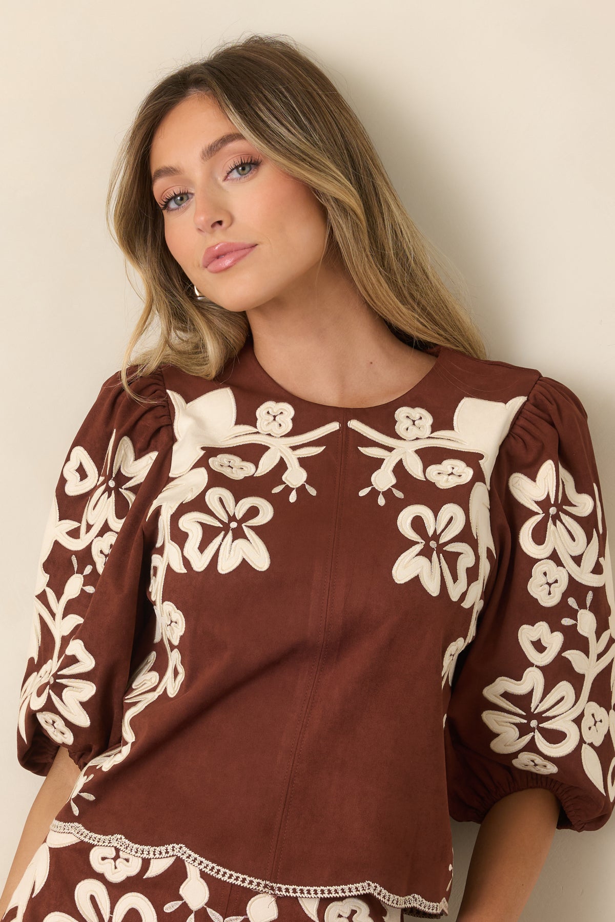 Ivory floral appliqués and embroidered detailing decorate the warm brown faux suede top.