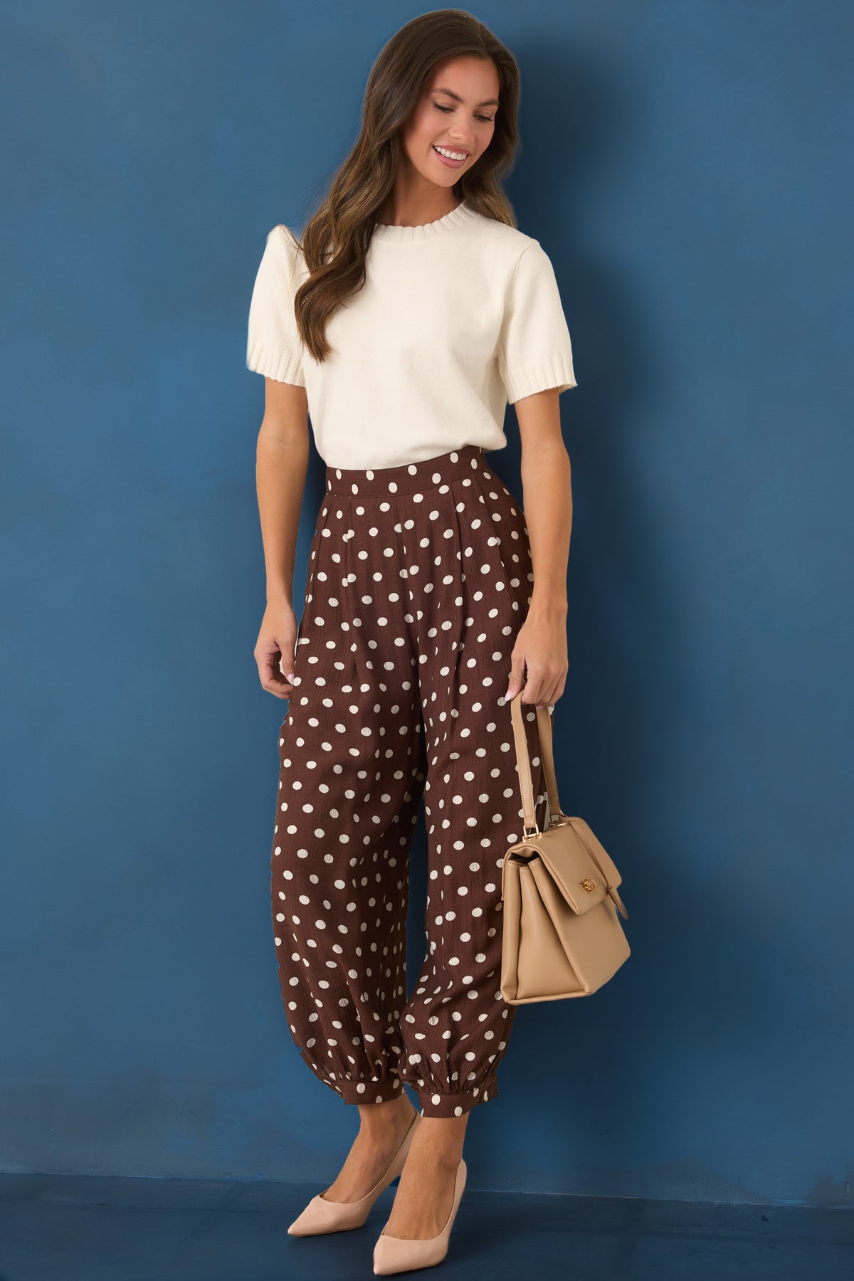 Rich brown pants with ivory polka dots, a high-rise waistband, front pleats, and voluminous balloon legs.