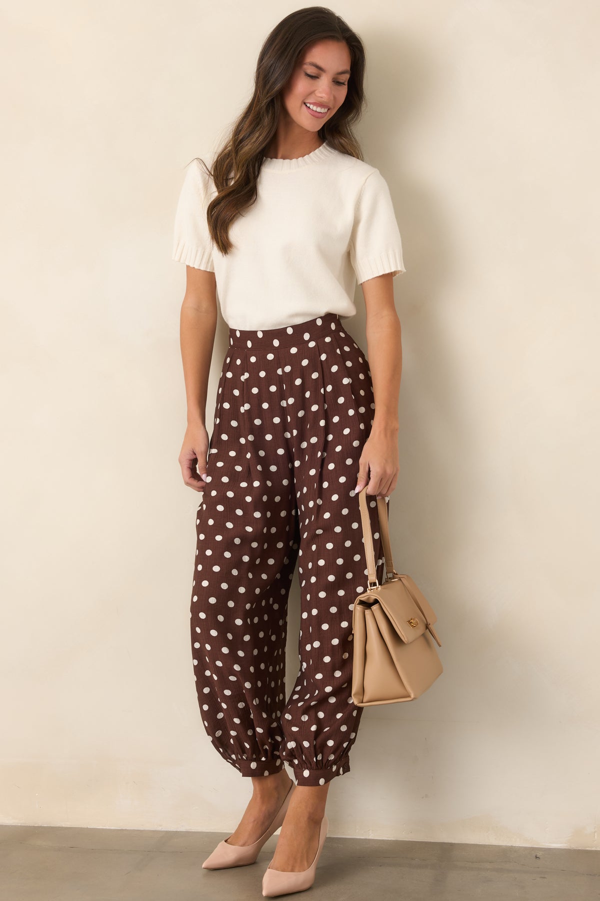 Rich brown pants with ivory polka dots, a high-rise waistband, front pleats, and voluminous balloon legs.