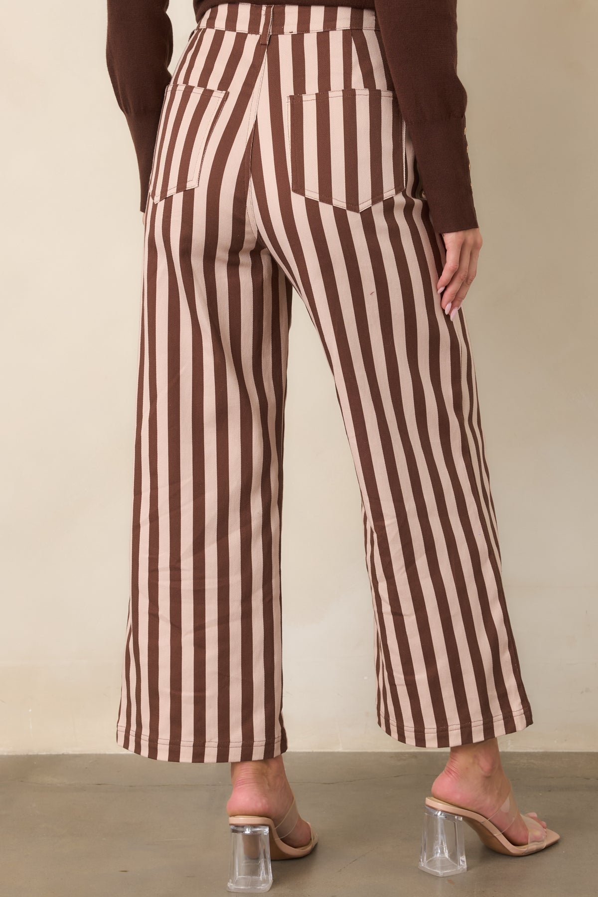 Rear view of the brown and ivory striped pants, highlighting the high-rise waist, rear pockets, vertical pattern, and cropped wide-leg silhouette.