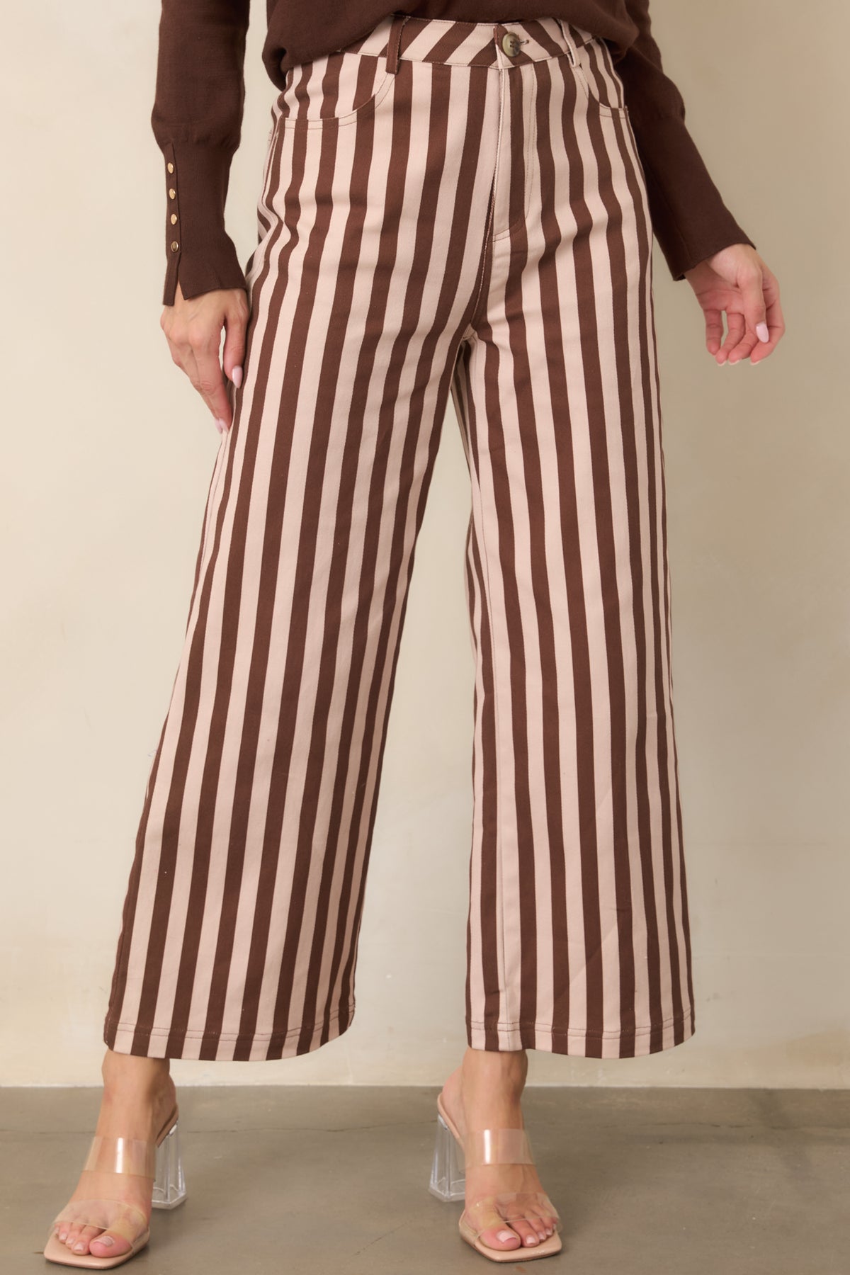 Close view of the brown and ivory striped pants, highlighting the tailored waistline, straight vertical pattern, and flowing wide legs.